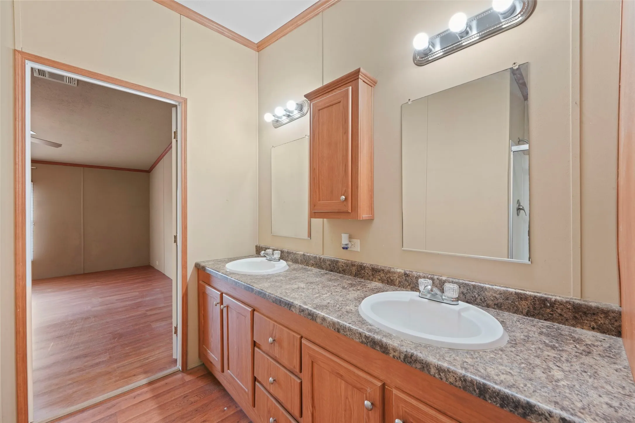 Bathroom vanity featuring dual inset sinks, a speckled countertop, and integrated wood-finish cabinetry