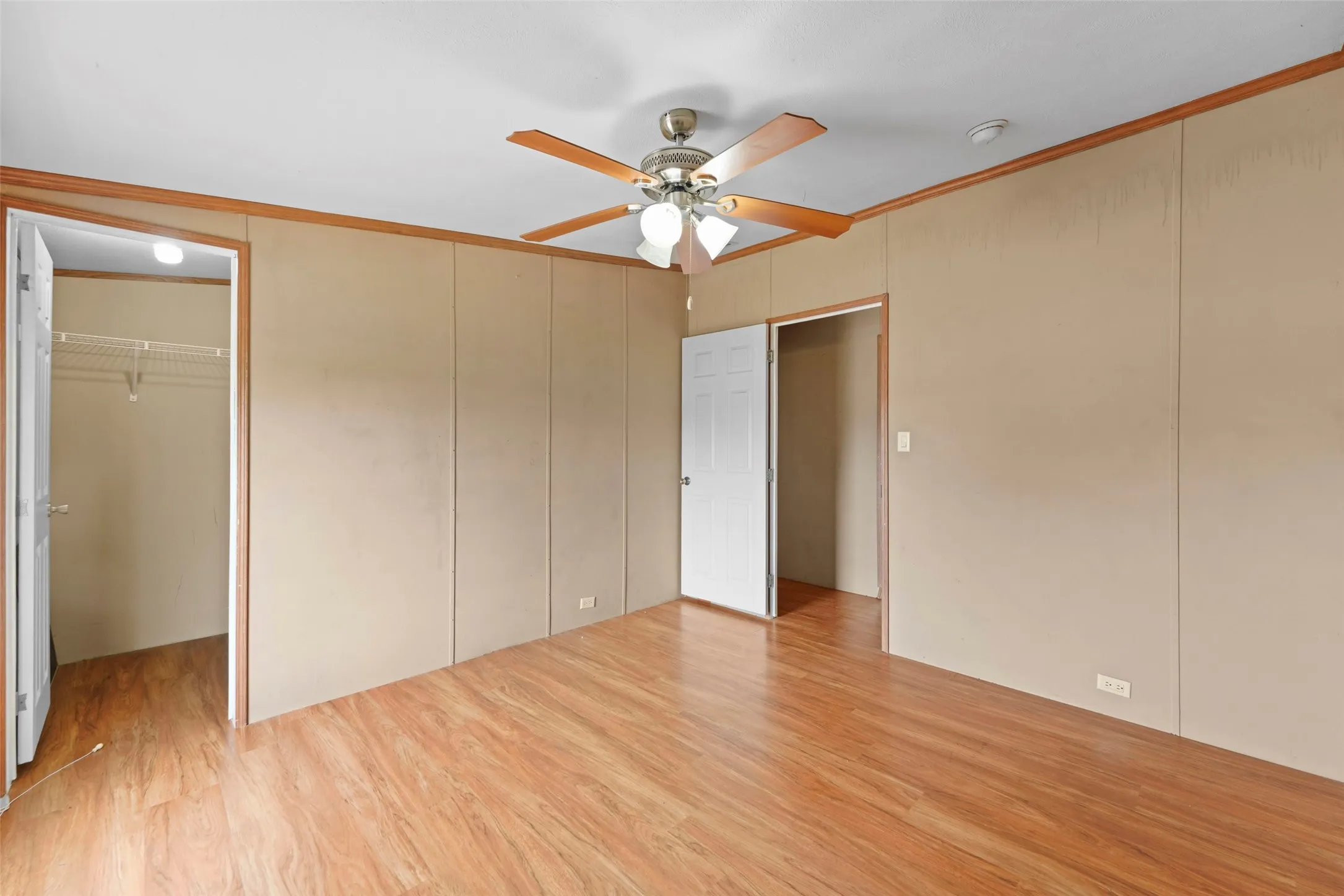 Spacious room featuring wood-finish flooring, a ceiling fan with integrated lighting, and multiple entryways