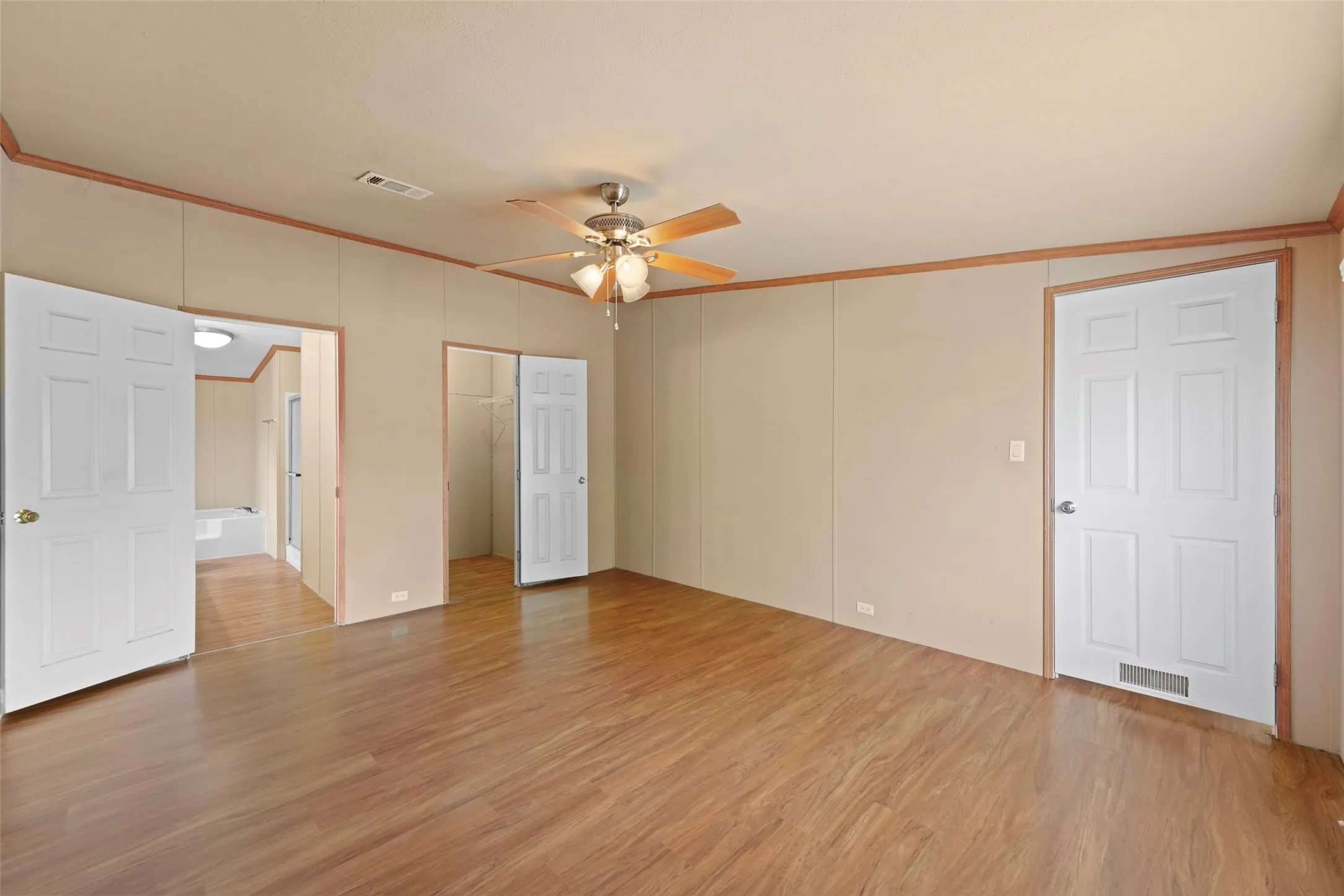 Spacious room featuring wood-finish flooring, a ceiling fan with light, and multiple paneled doors