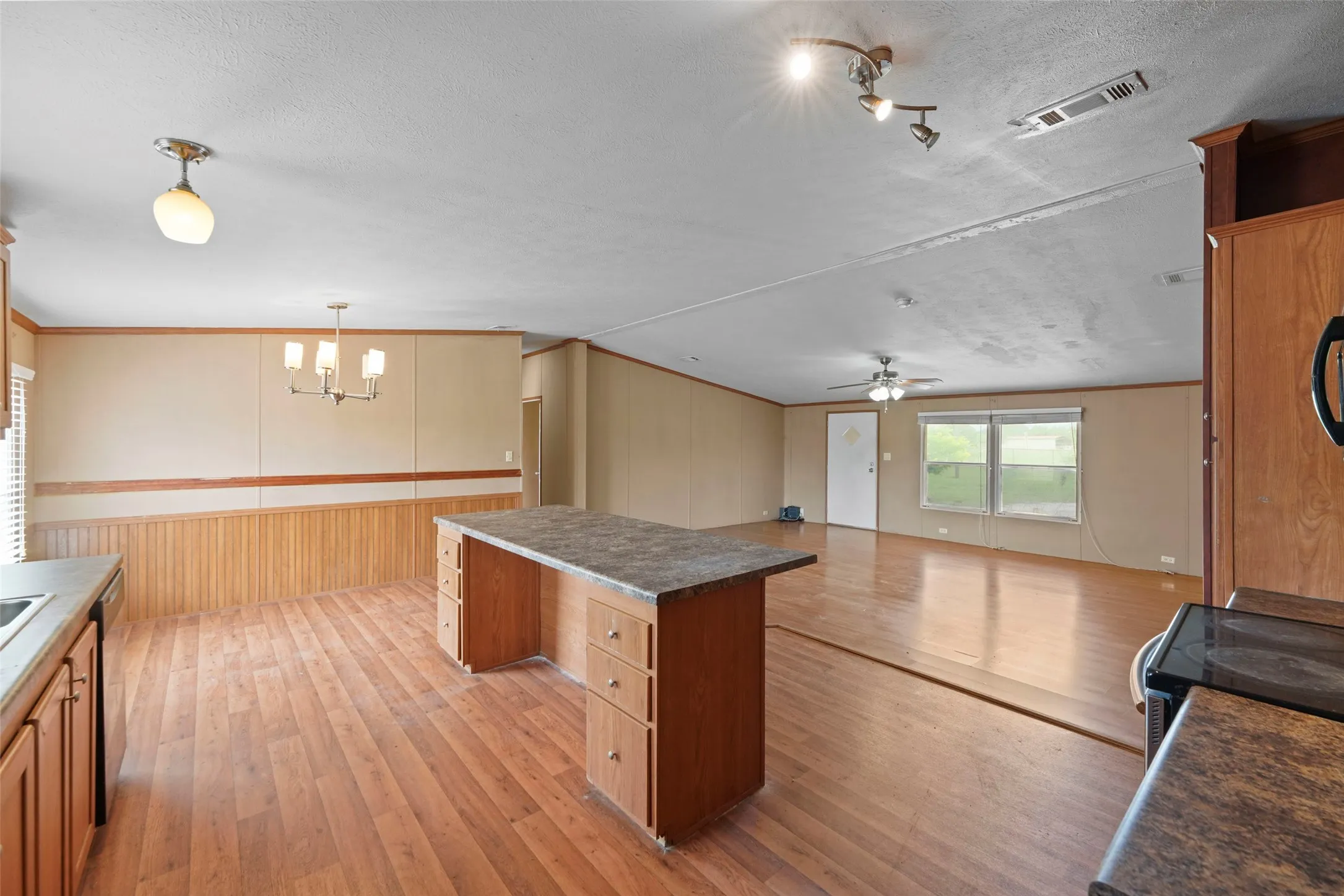 Open-concept living space with wood-finish flooring, a kitchen island with built-in cabinetry, and a dining area featuring wainscoting