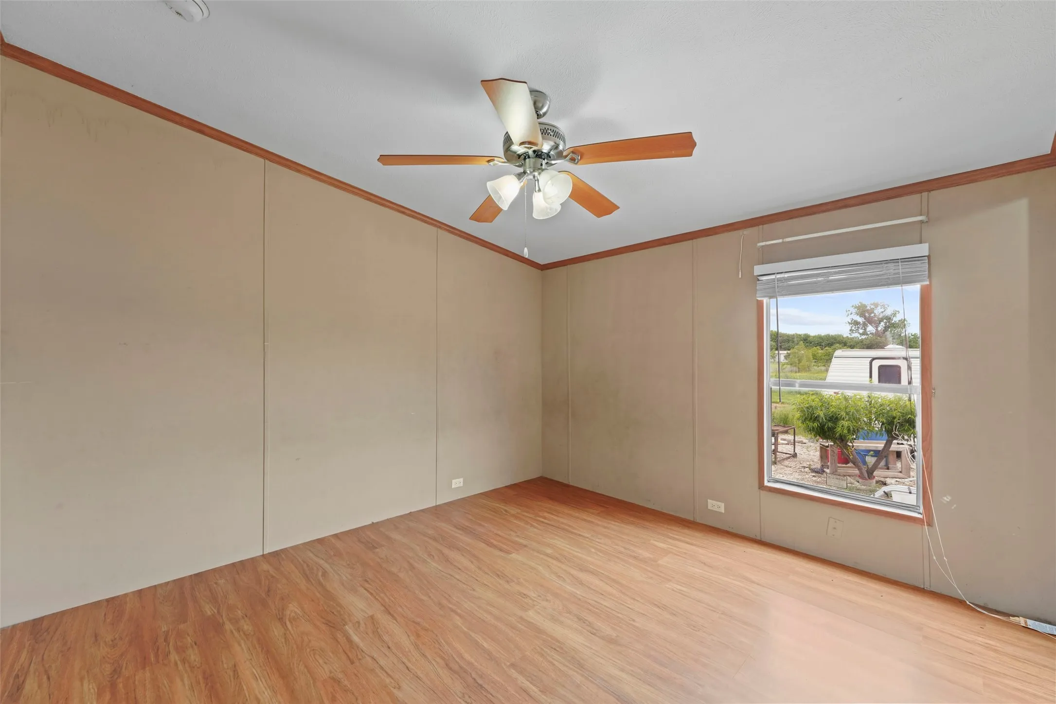 Spacious room featuring wood-finish flooring, a ceiling fan, and neutral-toned wall paneling