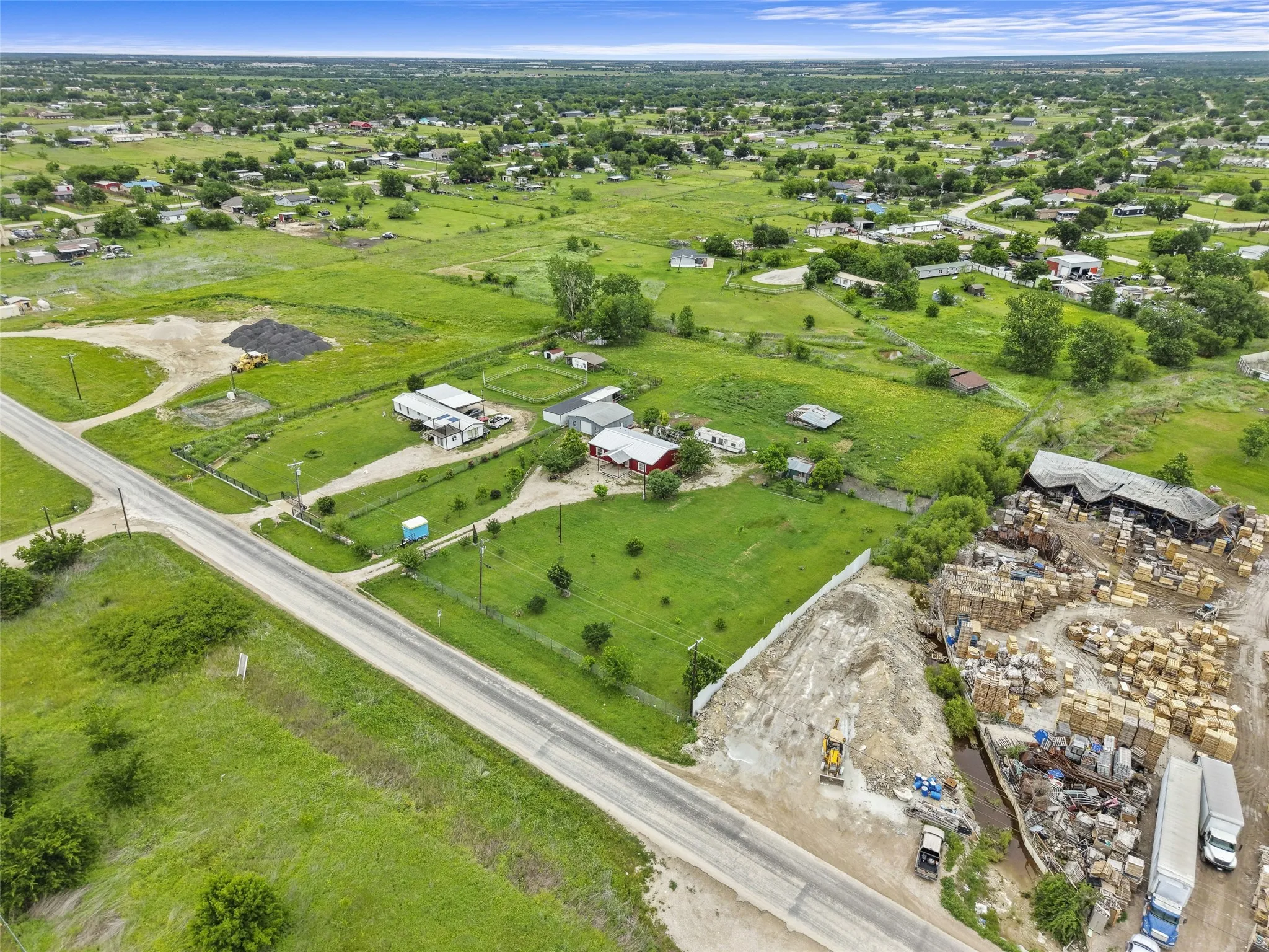 Expansive property featuring a paved road frontage, multiple structures, open green spaces, and a large commercial-style building