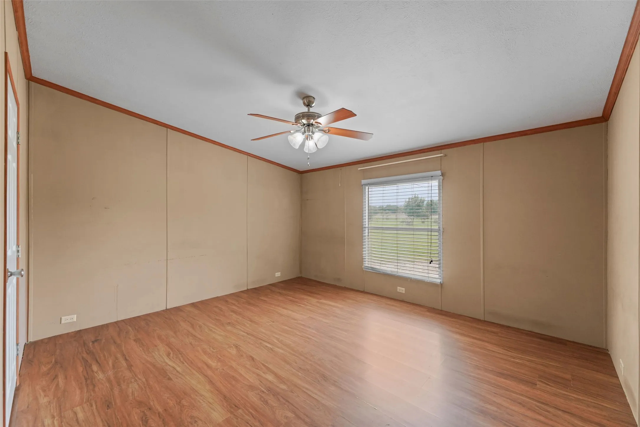 Spacious room featuring wood-finish flooring, a ceiling fan with light fixture, and a window with horizontal blinds