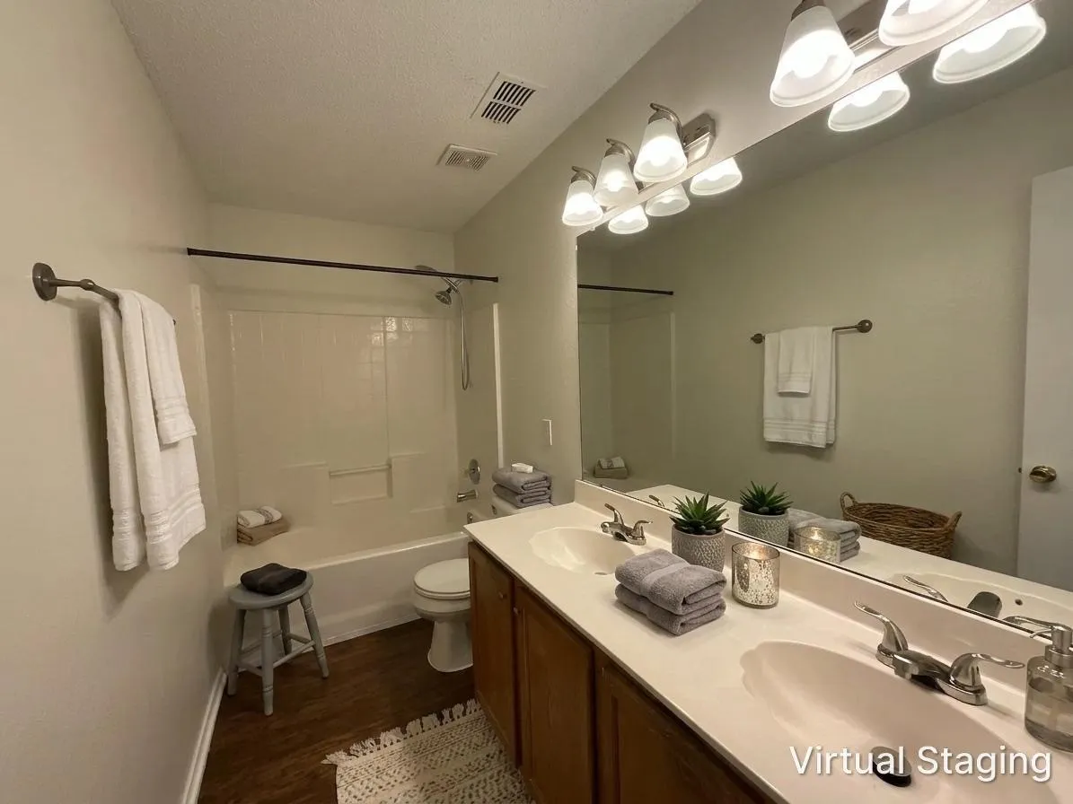 Full bathroom featuring a white tub/shower combination, wood-finish flooring, and a dual vanity with a white countertop