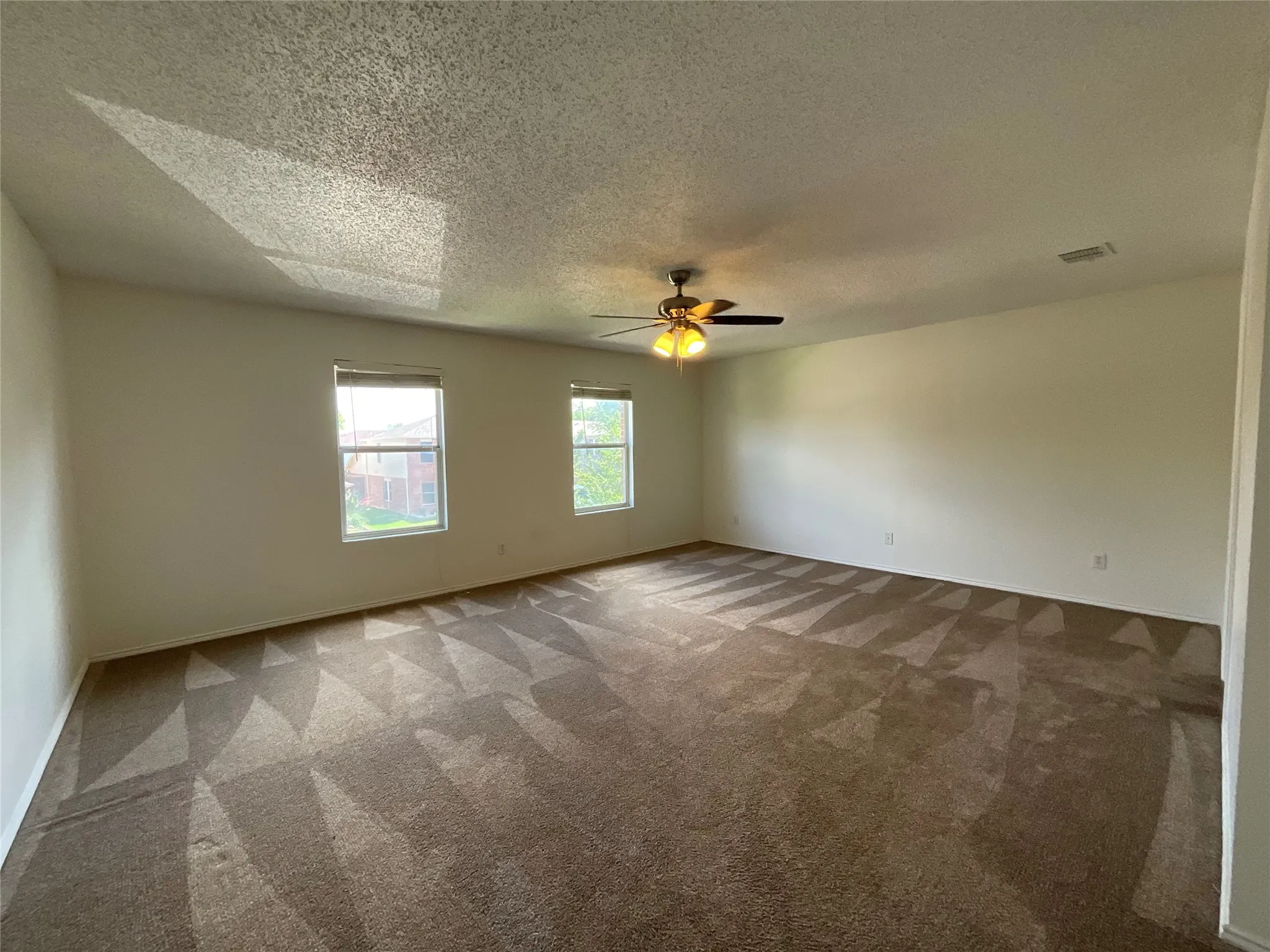 Spacious room featuring neutral carpeting with a patterned design, light-toned walls, and two windows with blinds