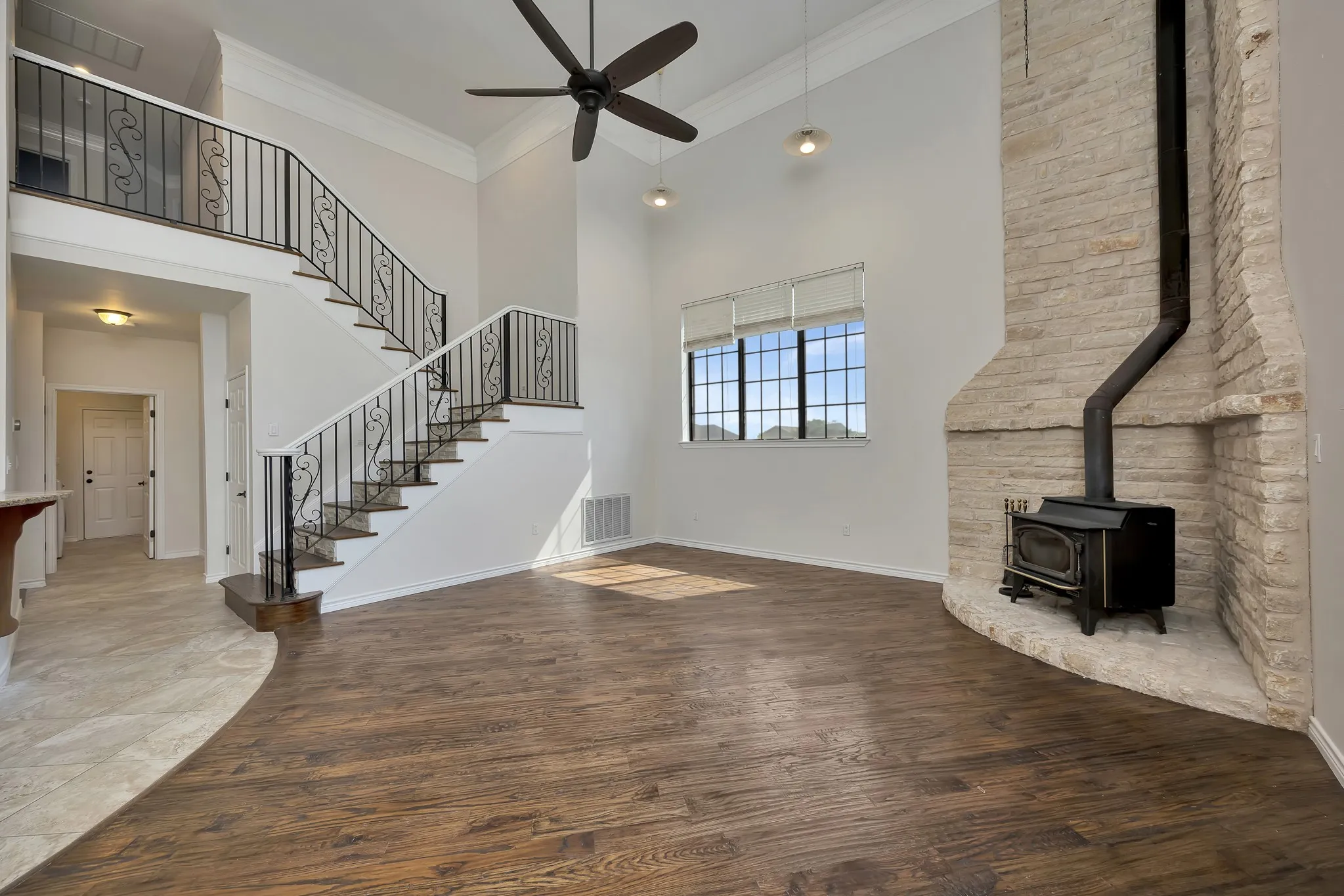 Unfurnished living room with a ceiling fan, a wood stove, a towering ceiling, stairs, and wood finished floors