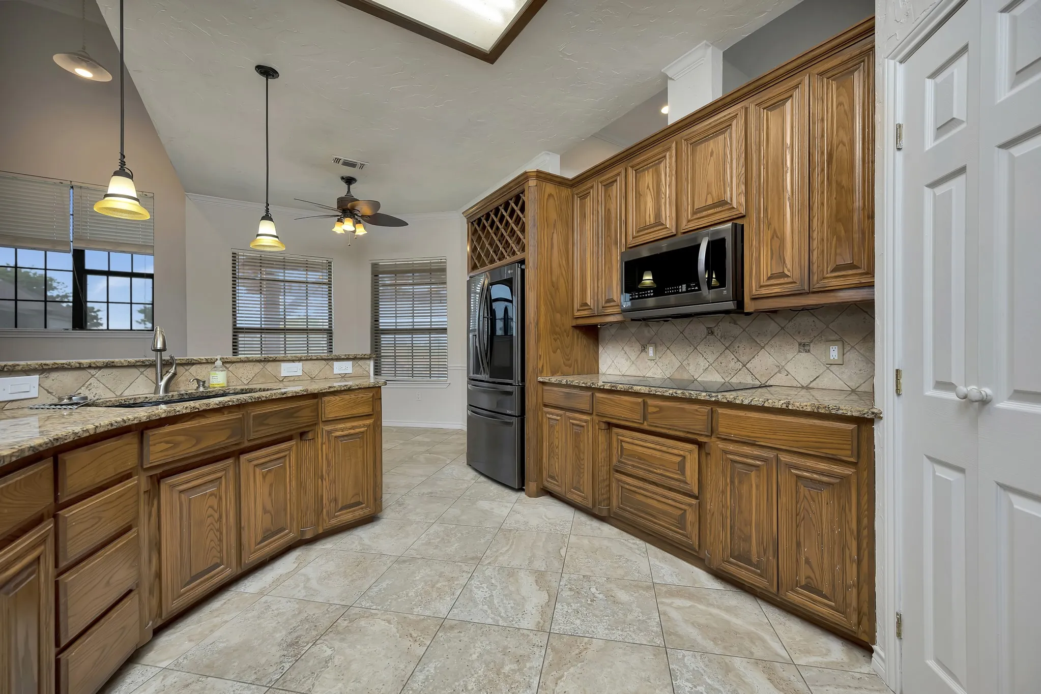 Kitchen featuring stainless steel microwave, smart refrigerator, brown cabinetry, backsplash, and a ceiling fan