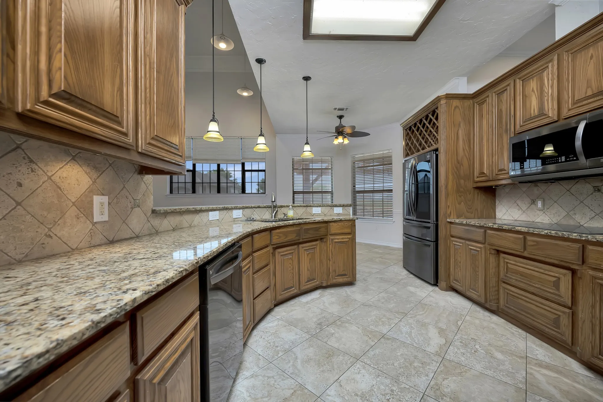 Kitchen with appliances with stainless steel finishes, brown cabinetry, ceiling fan, and a peninsula