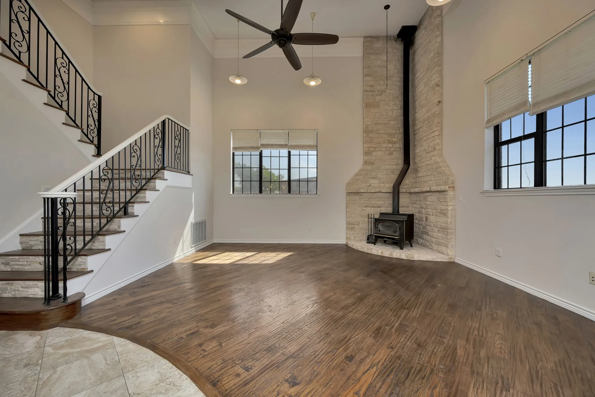 Unfurnished living room featuring a towering ceiling, a wood stove, a ceiling fan, plenty of natural light, and wood finished floors