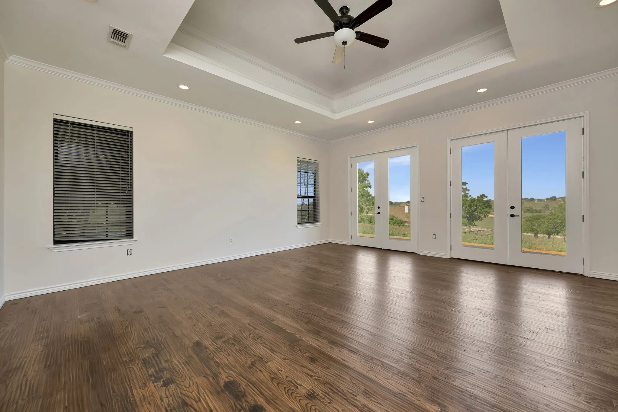 Empty room featuring french doors, a tray ceiling, crown molding, a ceiling fan, and dark wood-style floors