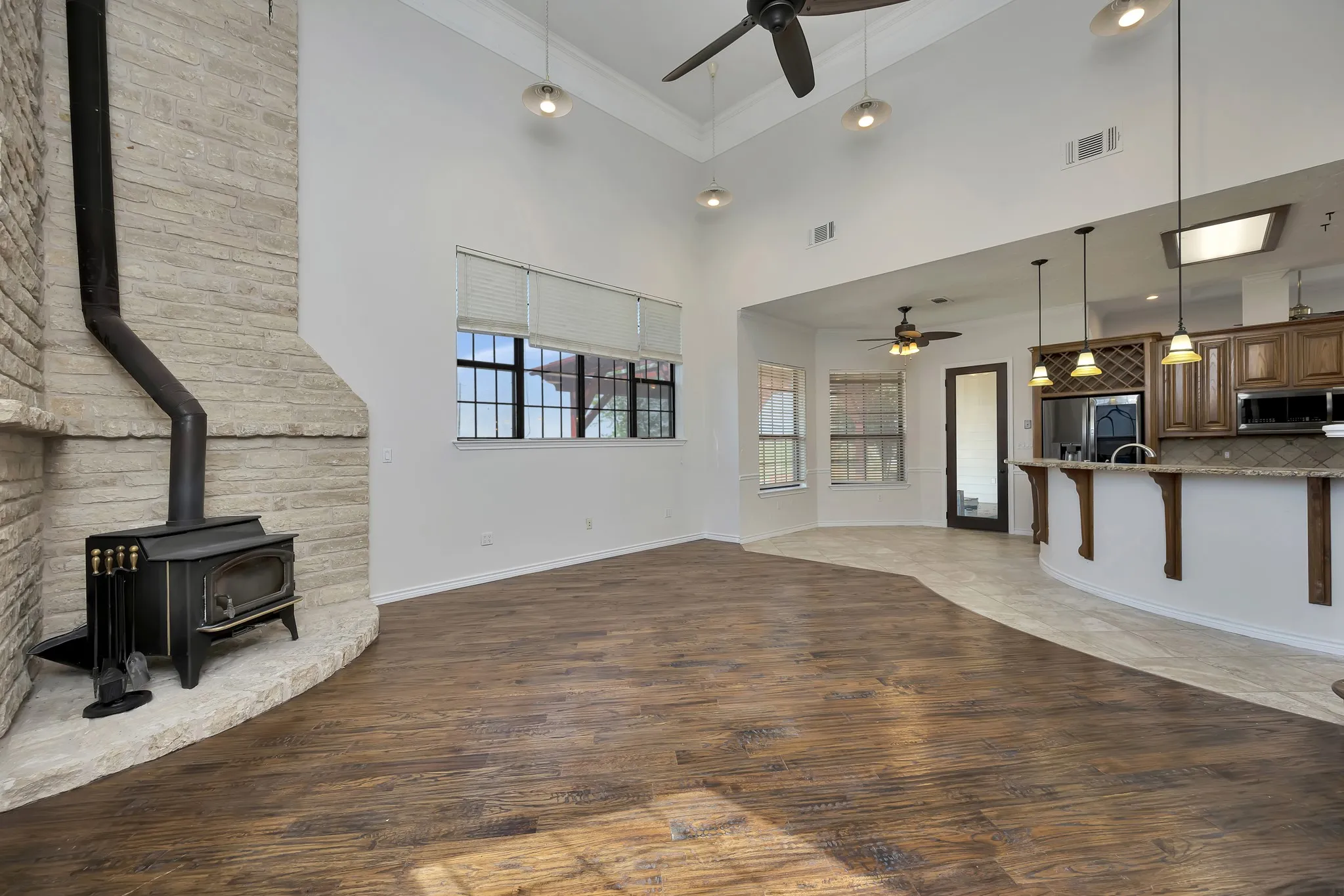 Unfurnished living room featuring a ceiling fan, a wood stove, wood finished floors, a high ceiling, and crown molding
