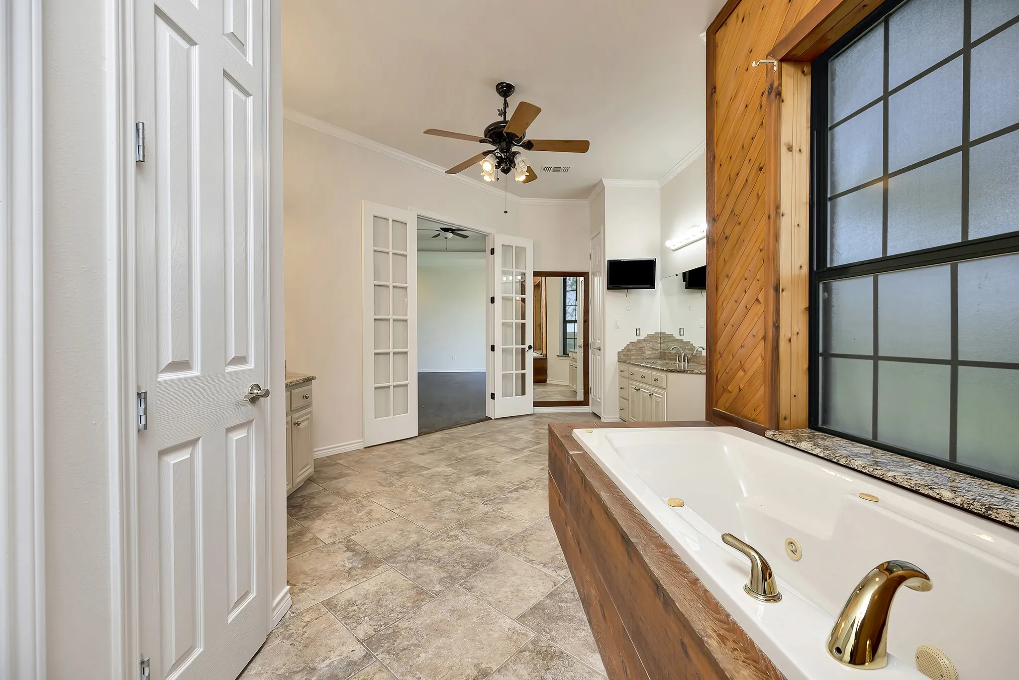 Full bath with french doors, a ceiling fan, crown molding, vanity, and a jetted tub