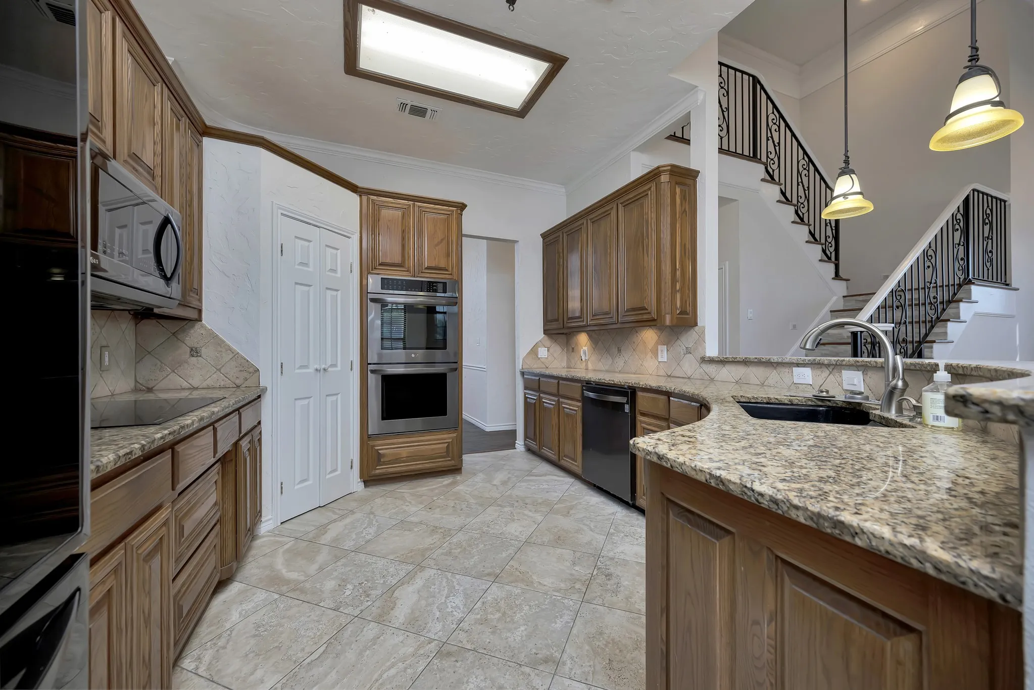 Kitchen with dishwashing machine, stainless steel double oven, black electric stovetop, light stone countertops, and tasteful backsplash