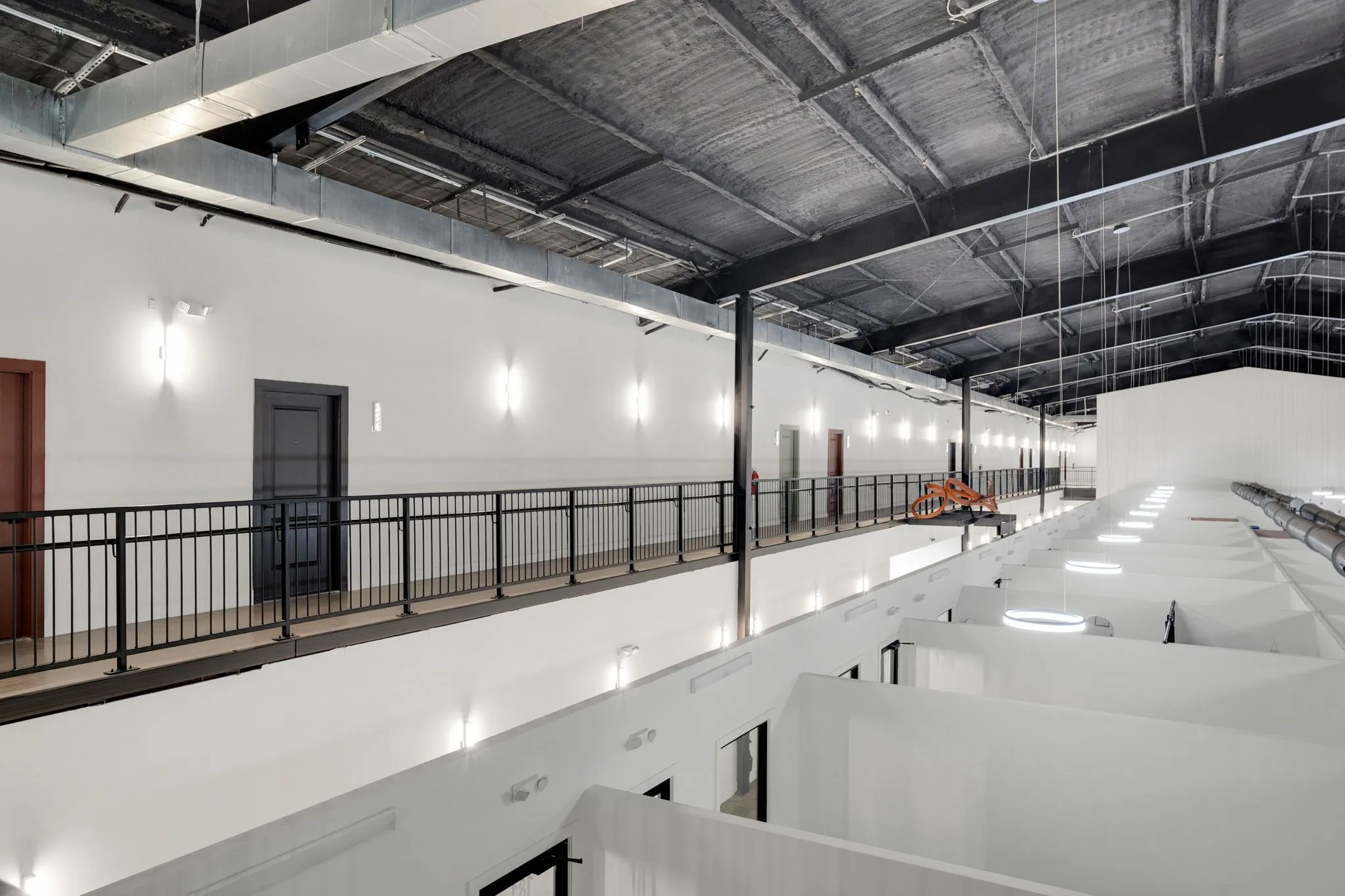 Multi-level interior featuring a black metal railing system, white walls with integrated lighting, exposed ceiling ductwork, and an industrial-style ceiling