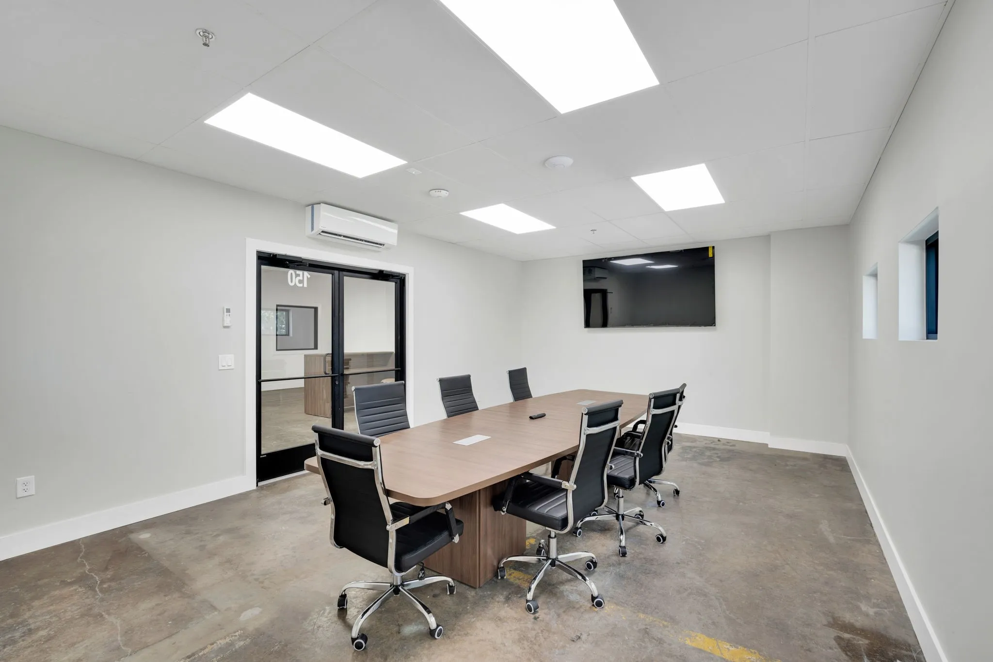 Conference room featuring a wood-finish table, polished concrete flooring, a wall-mounted display, and recessed lighting
