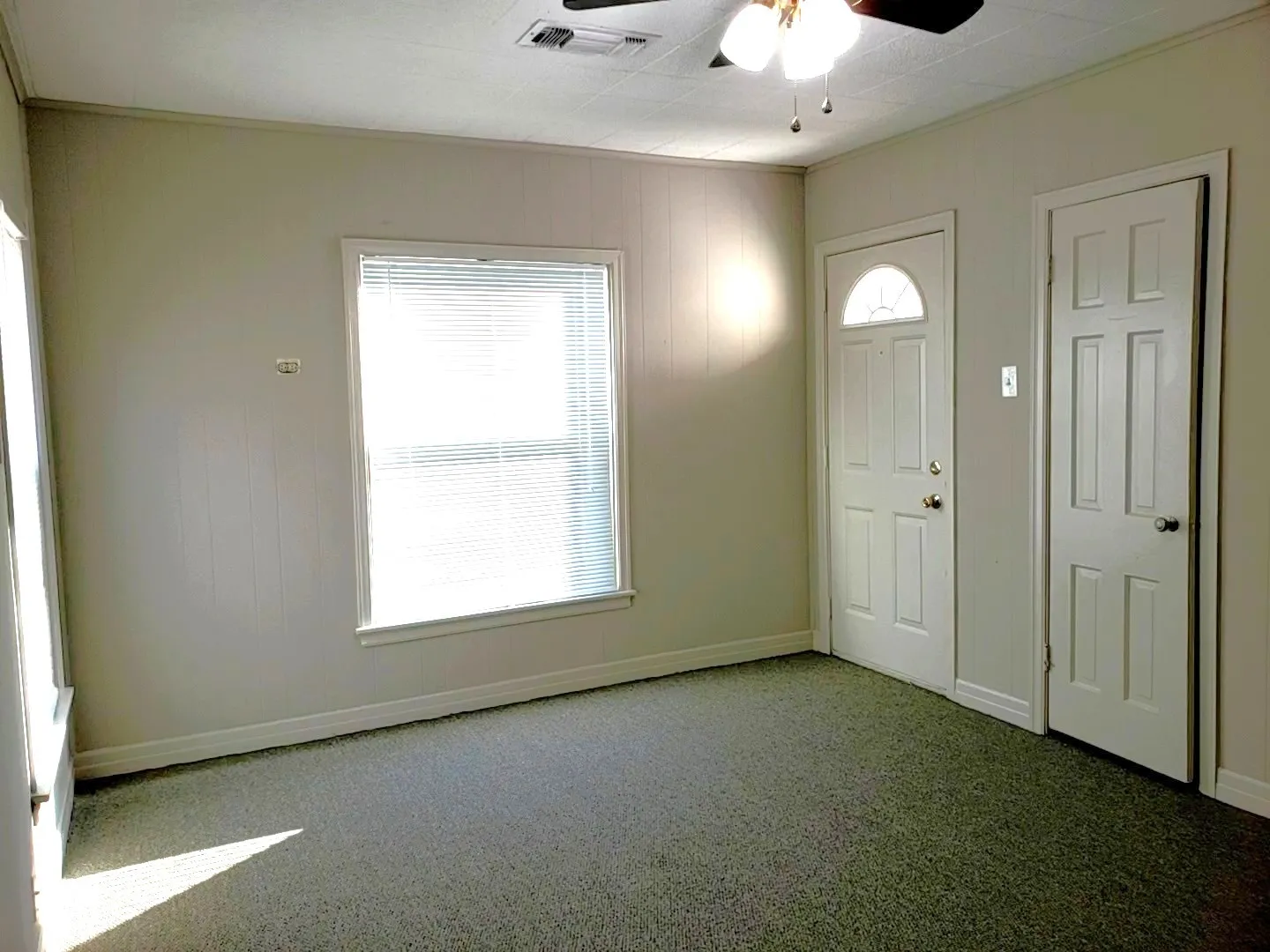 Carpeted interior space featuring a window with blinds, a half-moon glass panel door, a six-panel door, and a ceiling fan with integrated lighting