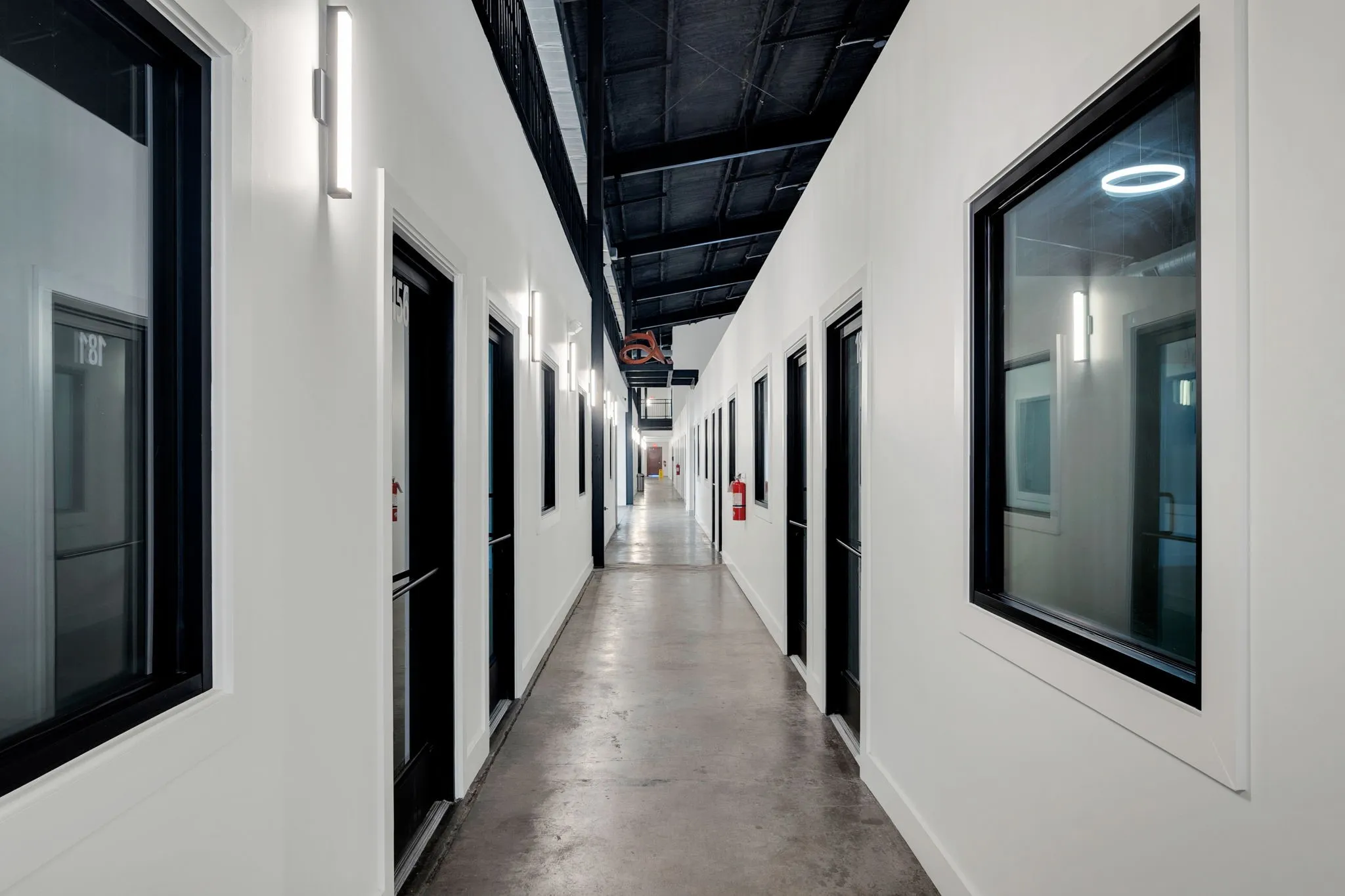 Corridor featuring white walls, black framed windows, and flush-mounted vertical lighting fixtures
