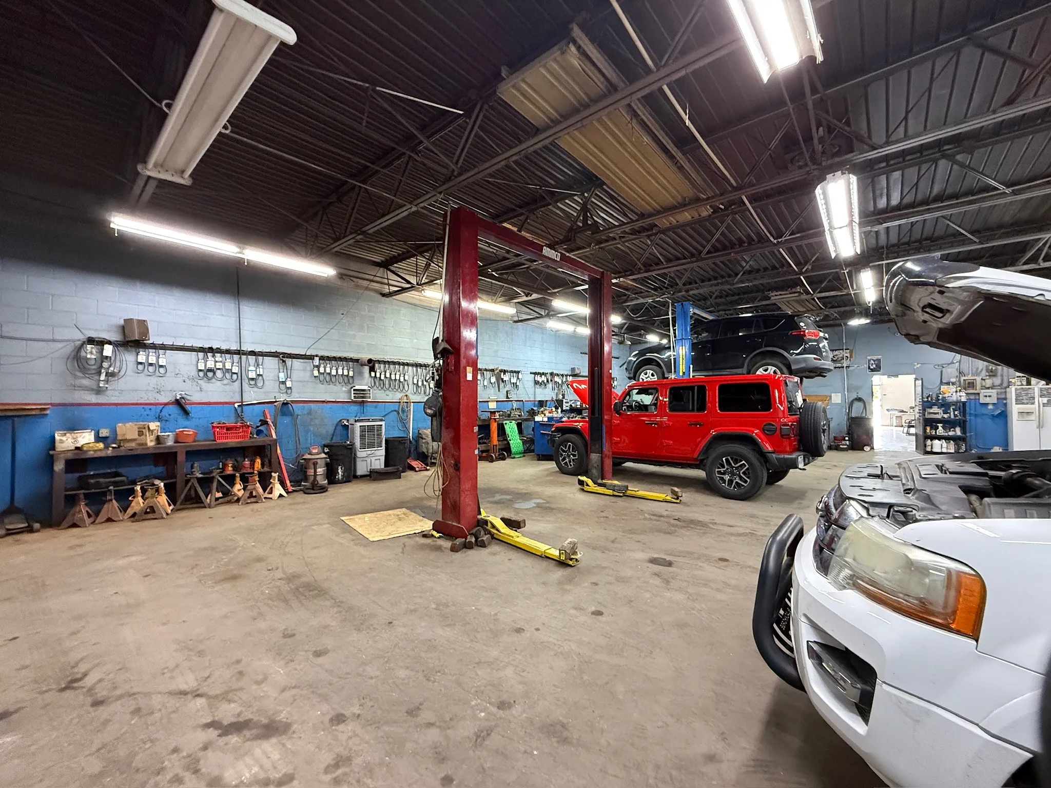 Industrial-style building featuring a concrete floor, exposed structural ceiling, multiple overhead fluorescent light fixtures, and a two-post vehicle lift