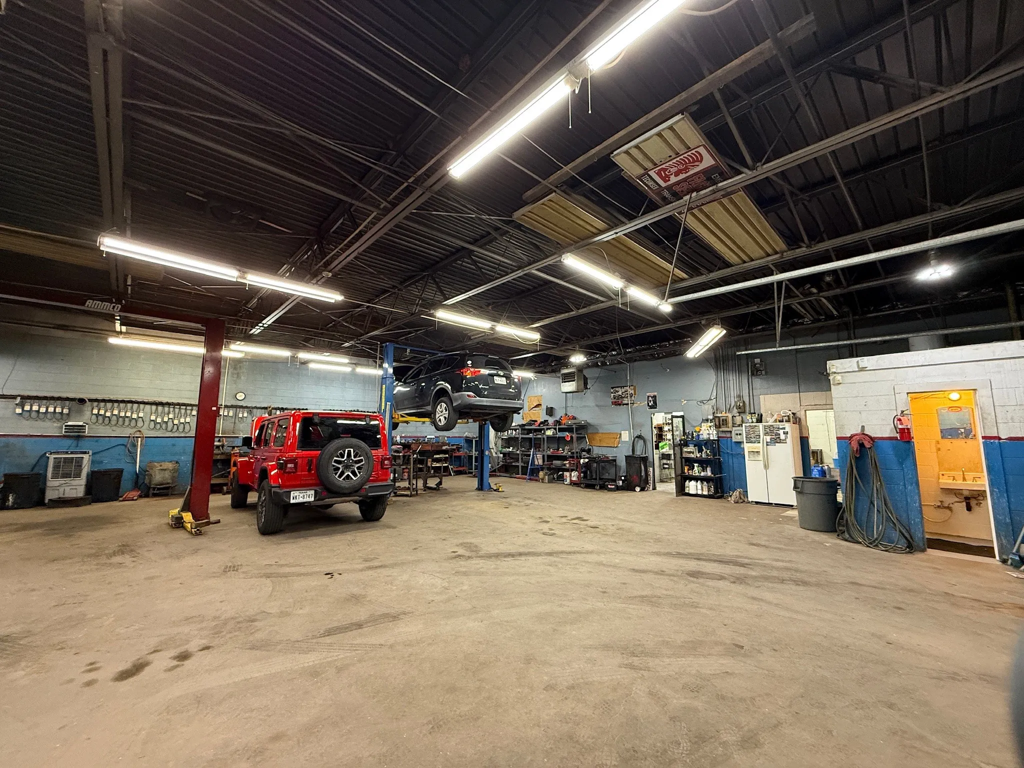 Industrial-style interior featuring high ceilings with exposed trusses, multiple overhead fluorescent light fixtures, and a concrete floor