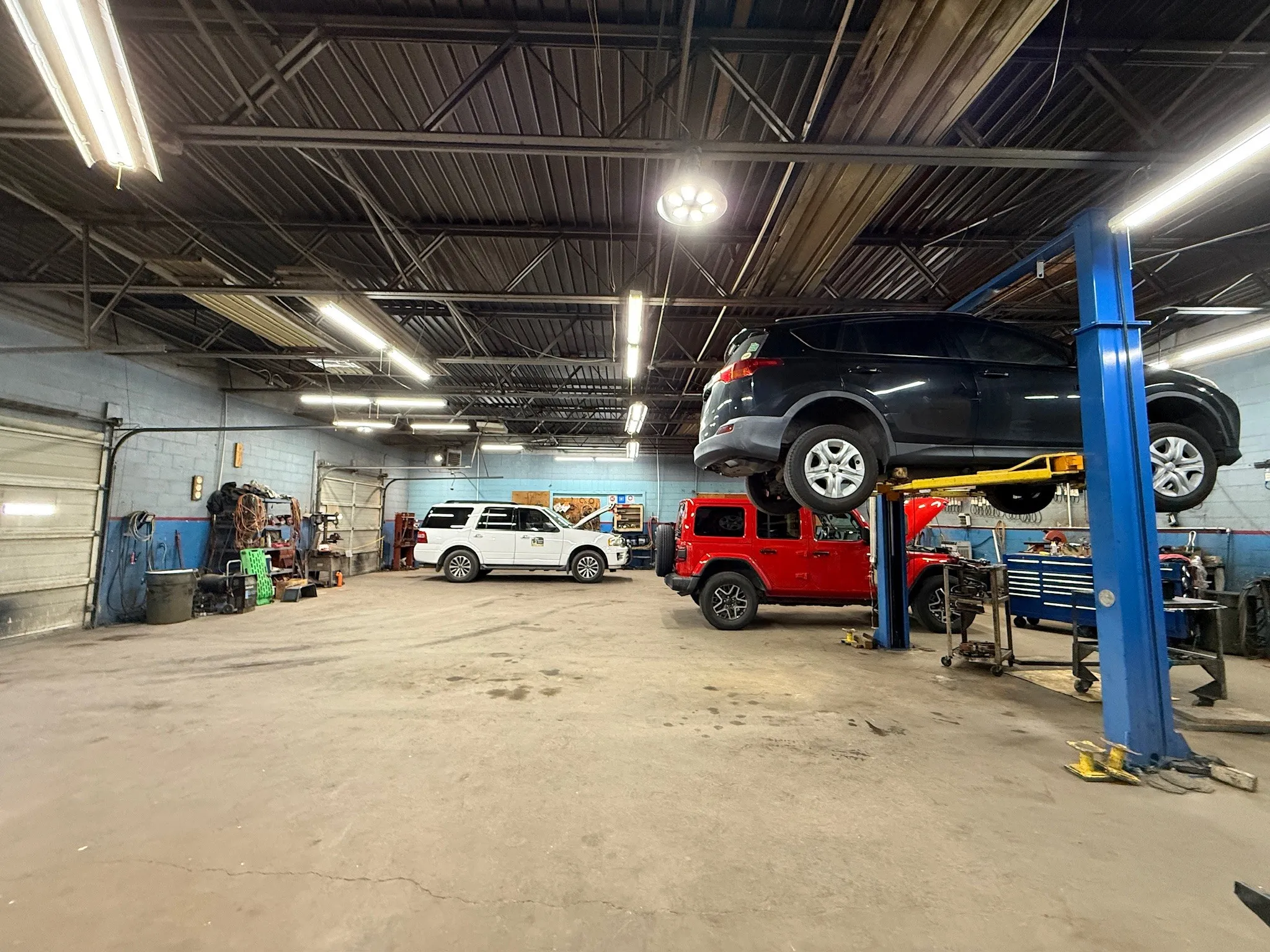 Spacious automotive service bay featuring a vehicle lift, concrete flooring, and overhead fluorescent lighting