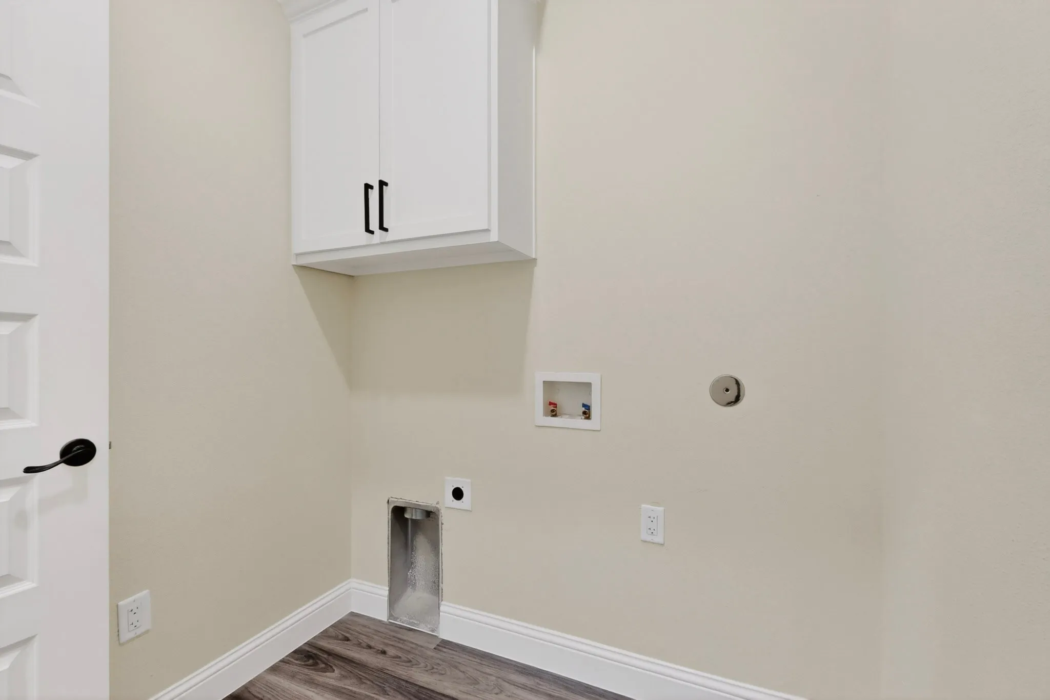 Dedicated laundry space featuring white upper cabinetry with dark hardware, a panel door with dark hardware, wood-finish flooring, and light wall paint