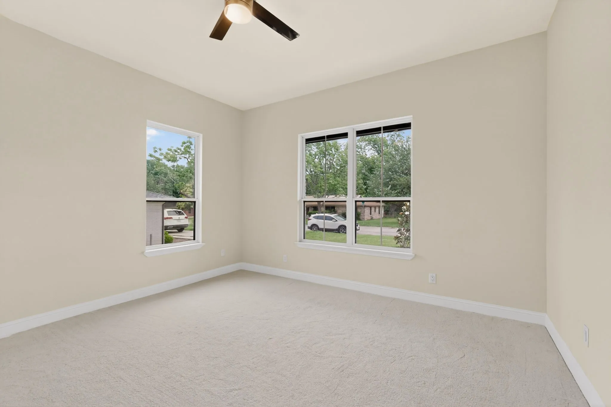 Neutral-toned room featuring a ceiling fan with light, two windows, wall-to-wall carpeting, and baseboard trim