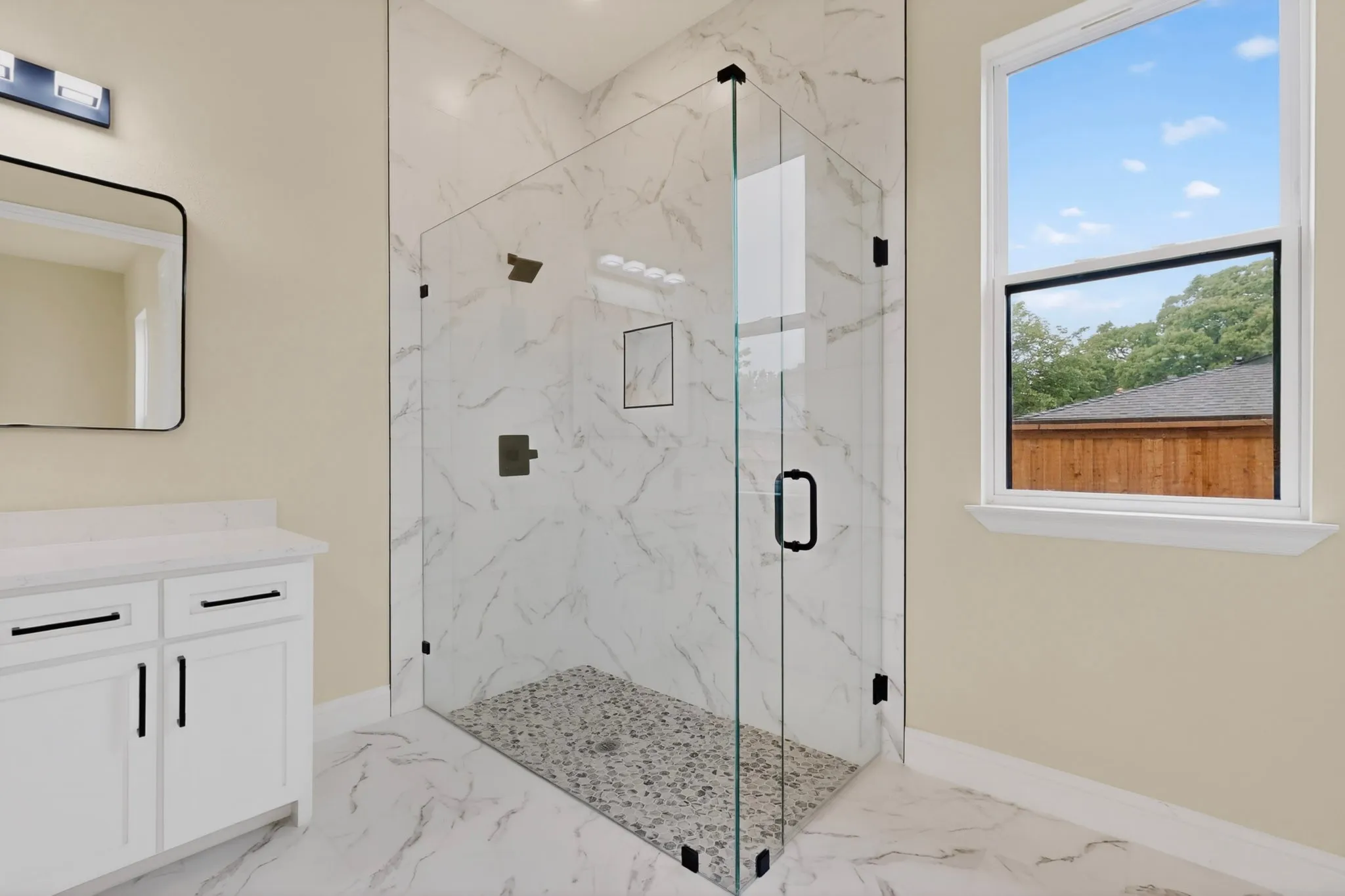 Glass-enclosed shower featuring white marble-look tile walls and a pebble-stone floor