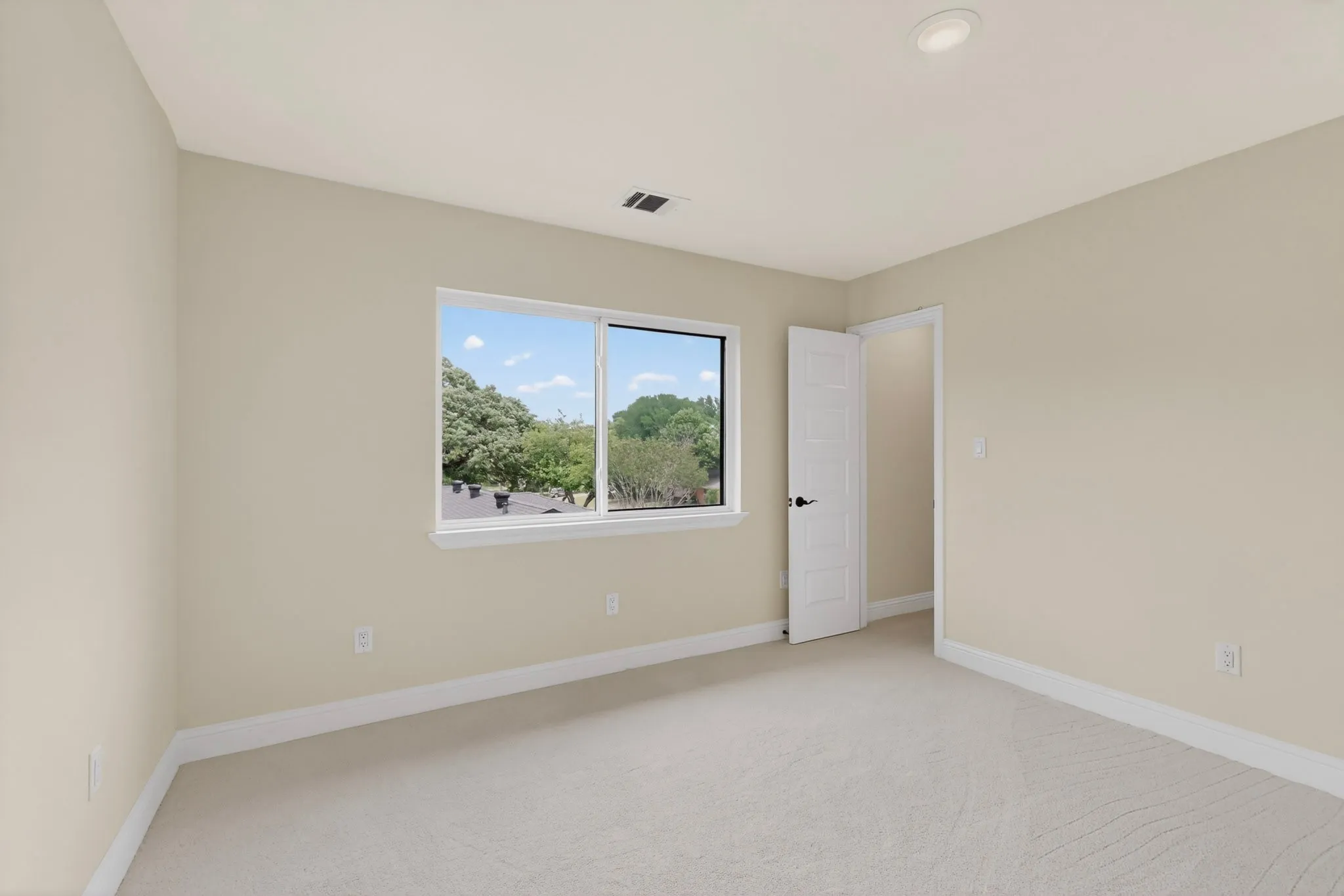 Spacious room featuring neutral carpeting, a large window, recessed lighting, and a white paneled door with dark hardware