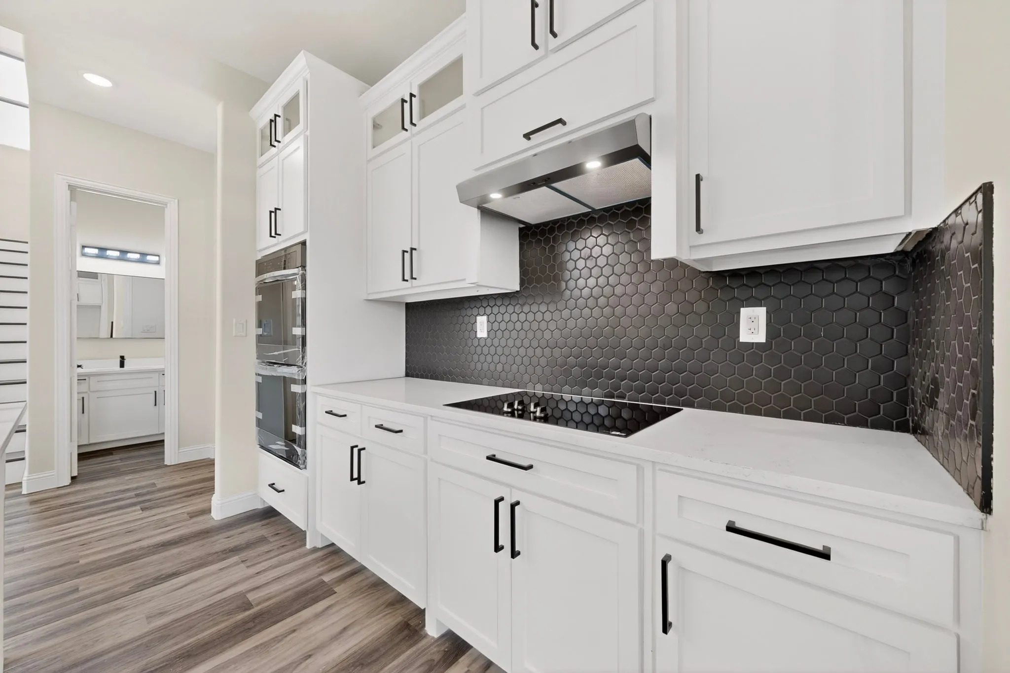 Kitchen featuring white cabinetry with black hardware, white countertops, and a black hexagonal tile backsplash