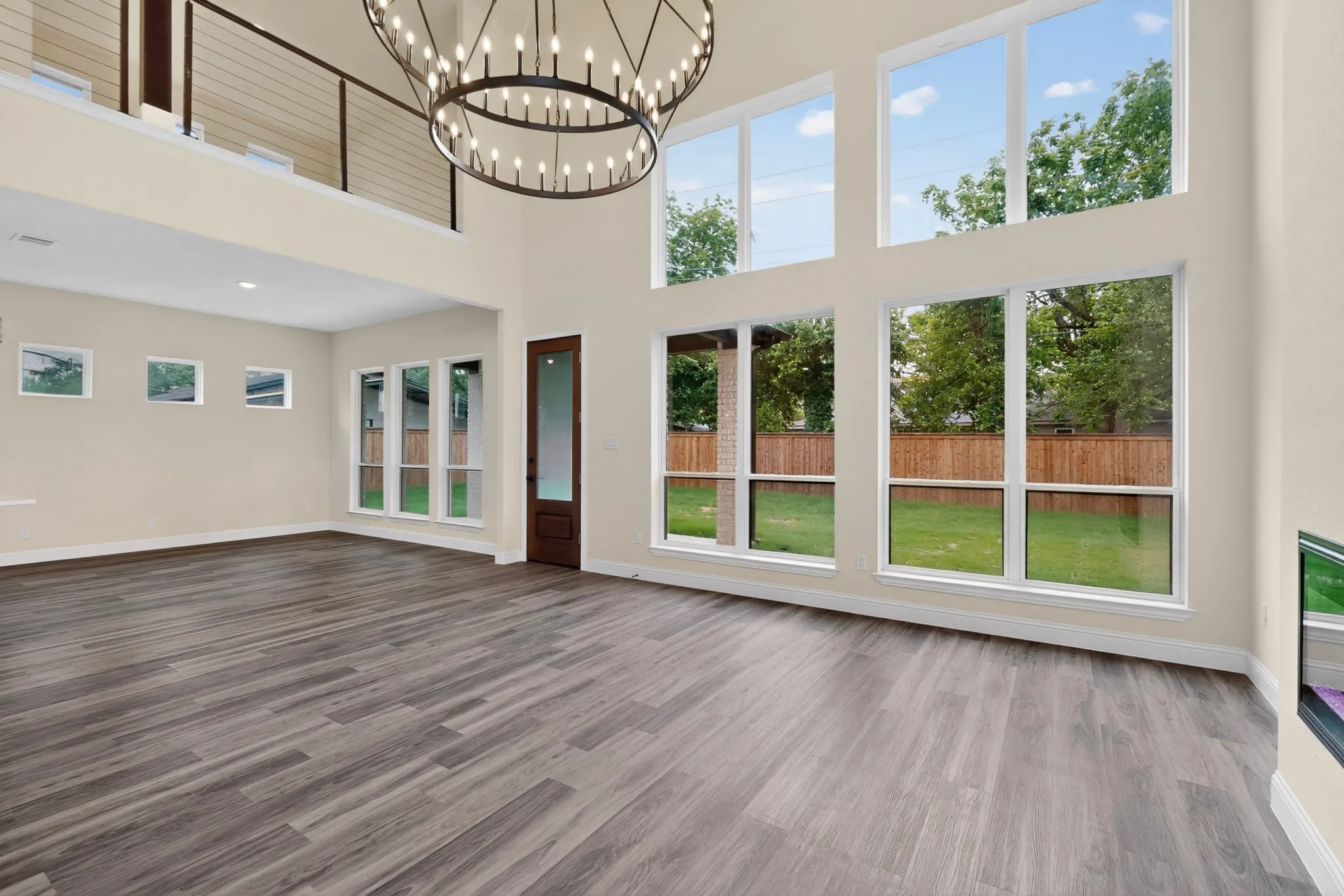Vaulted living space featuring an oversized chandelier, a two-story window array overlooking a fenced backyard, and wood-finish flooring