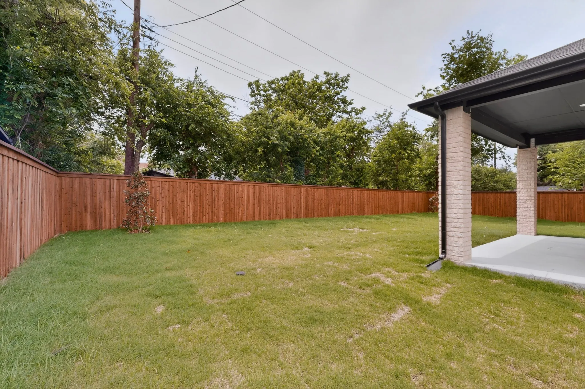 Spacious backyard featuring a manicured lawn, full wood privacy fencing, and a covered concrete patio with brick-clad columns