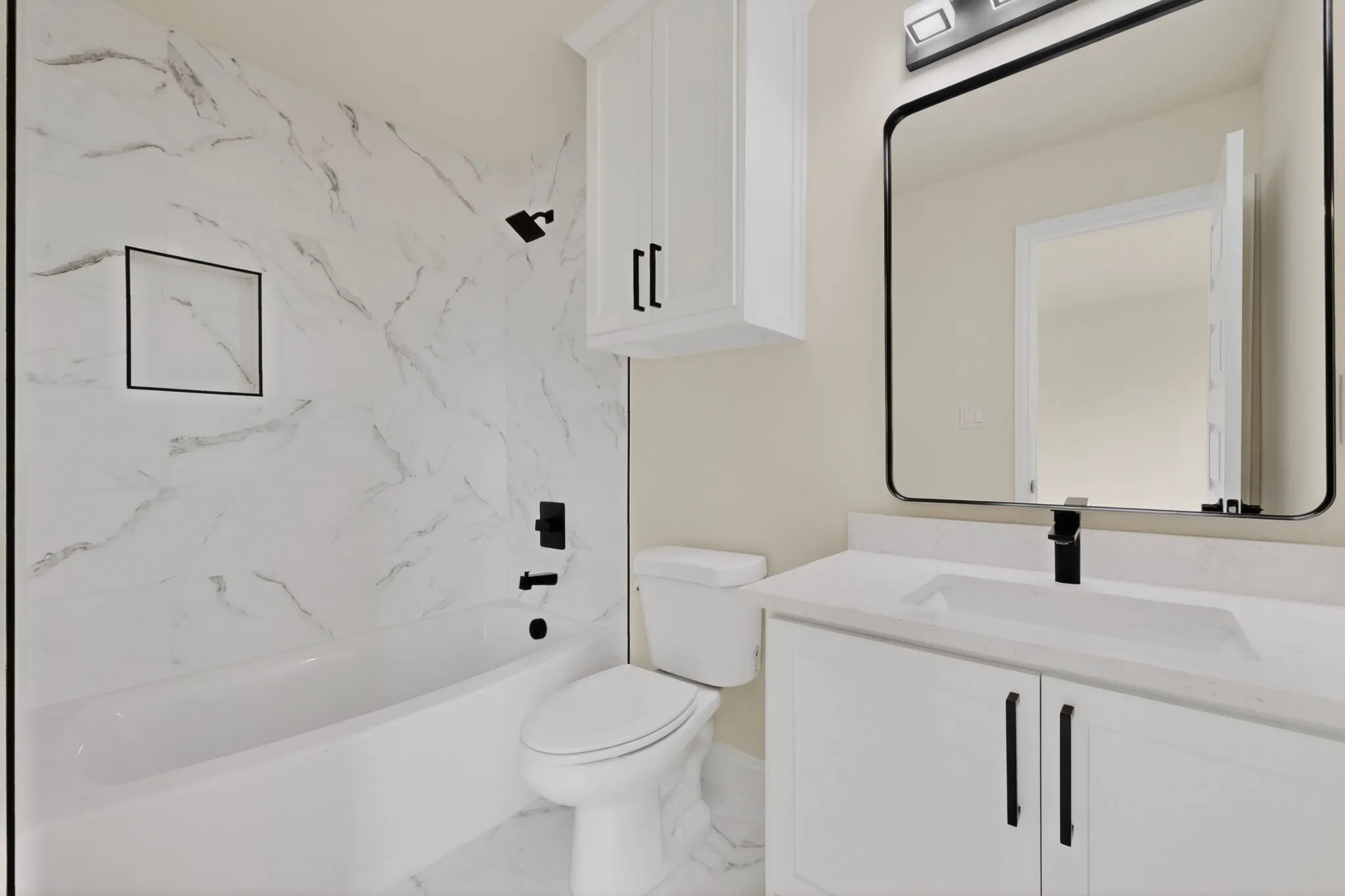 Full bathroom featuring a white tub with matte black fixtures, a built-in shower niche, and white marble-look wall tiling