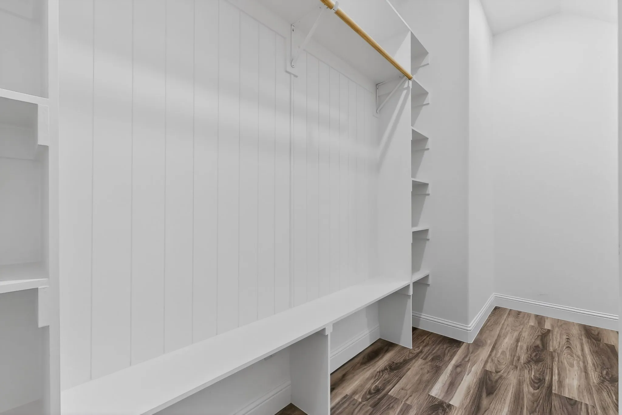 Built-in white cabinetry featuring beadboard paneling, multiple shelving units, a hanging rod, and bench seating