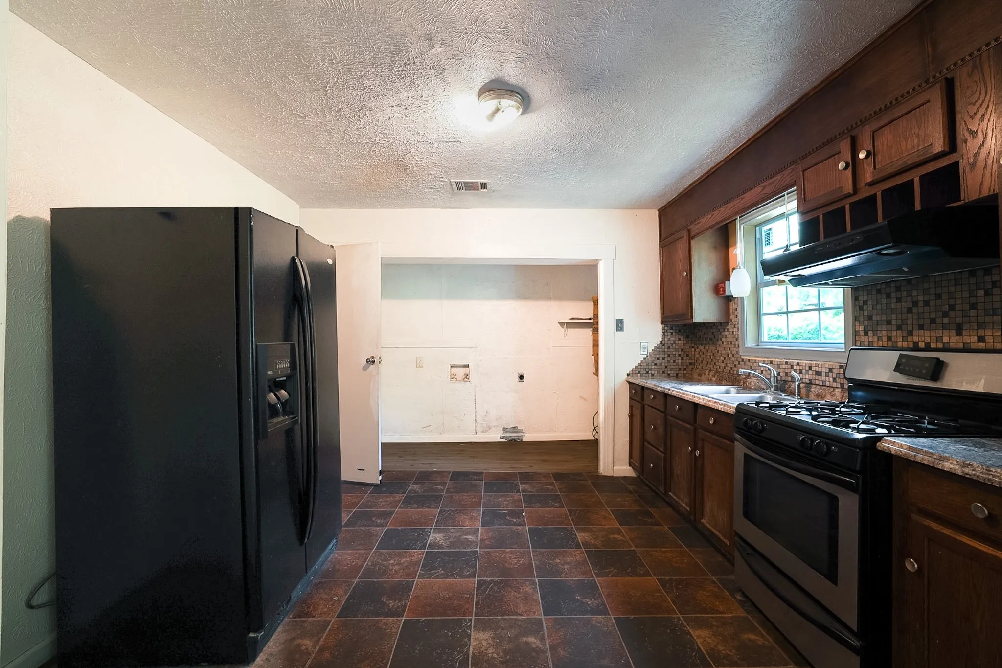 Kitchen featuring wood cabinetry, mosaic tile backsplash, and a black gas range with an overhead exhaust fan