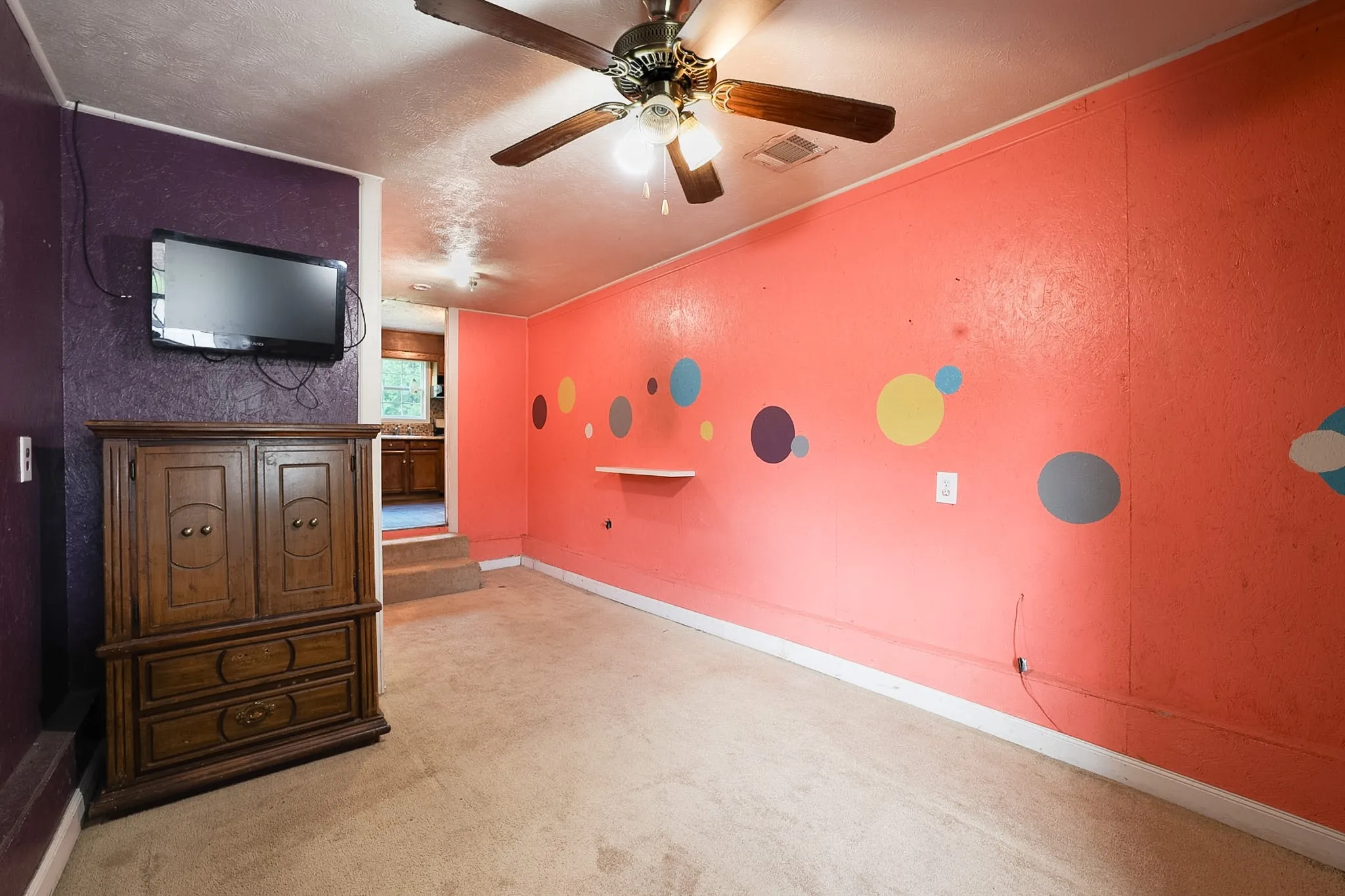Interior room featuring textured walls with a contrasting accent wall, ceiling fan with light fixture, and carpeted flooring