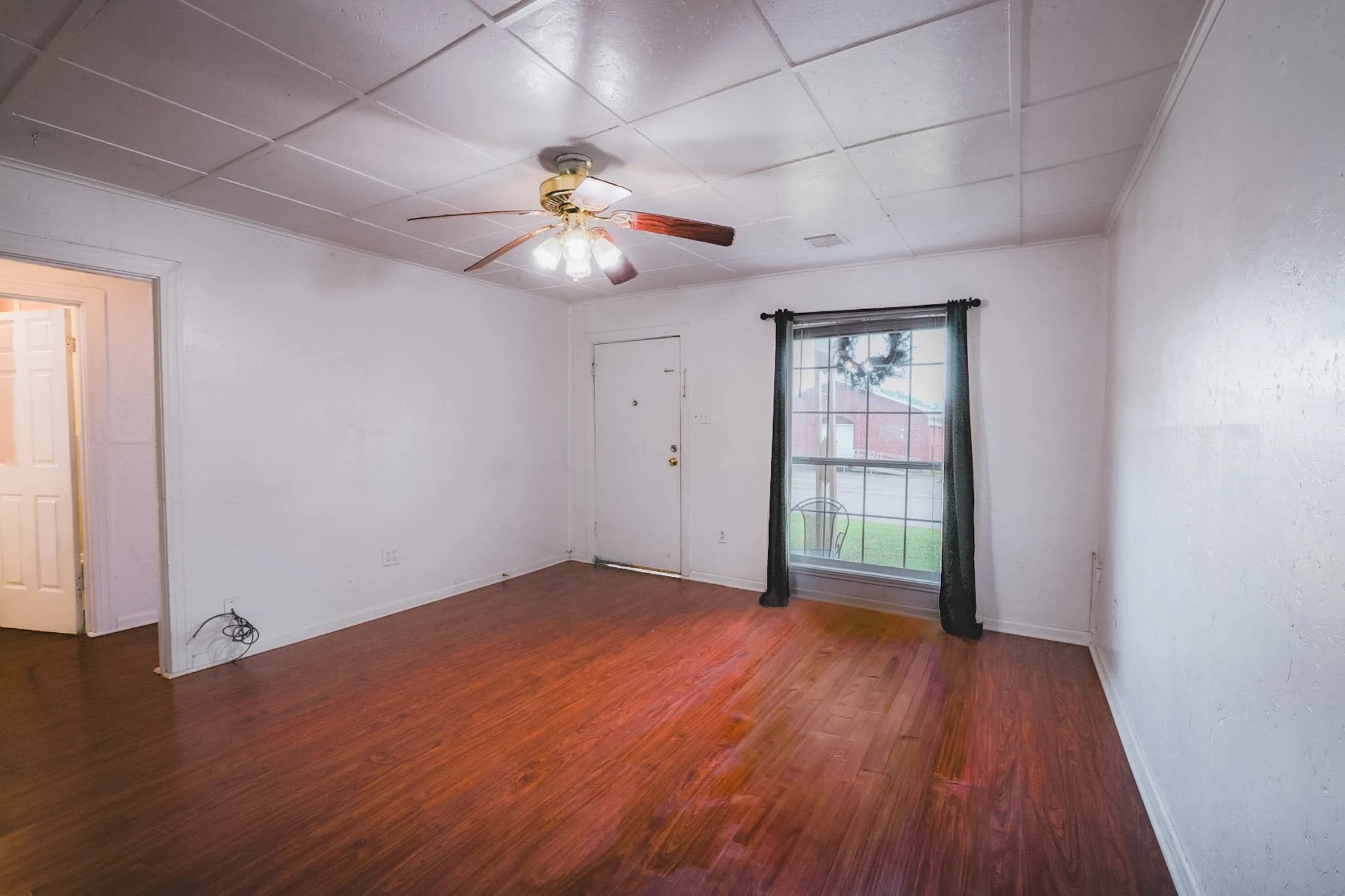 Spacious room featuring wood-finish flooring, white walls, and a ceiling fan with integrated lighting