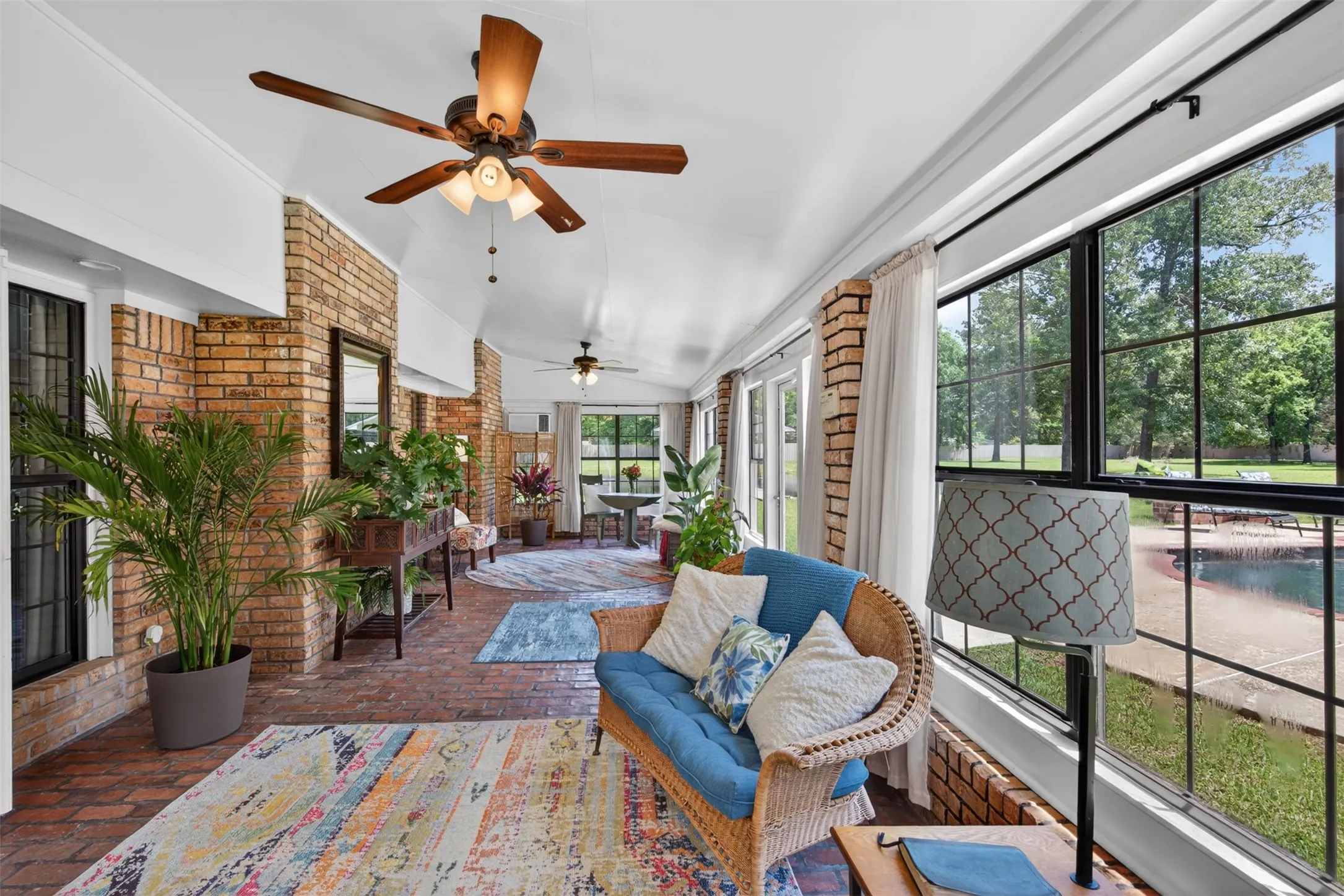 Enclosed sunroom featuring brick walls, a vaulted white ceiling, multiple ceiling fans with integrated lighting, and large grid-pattern windows overlooking a pool area