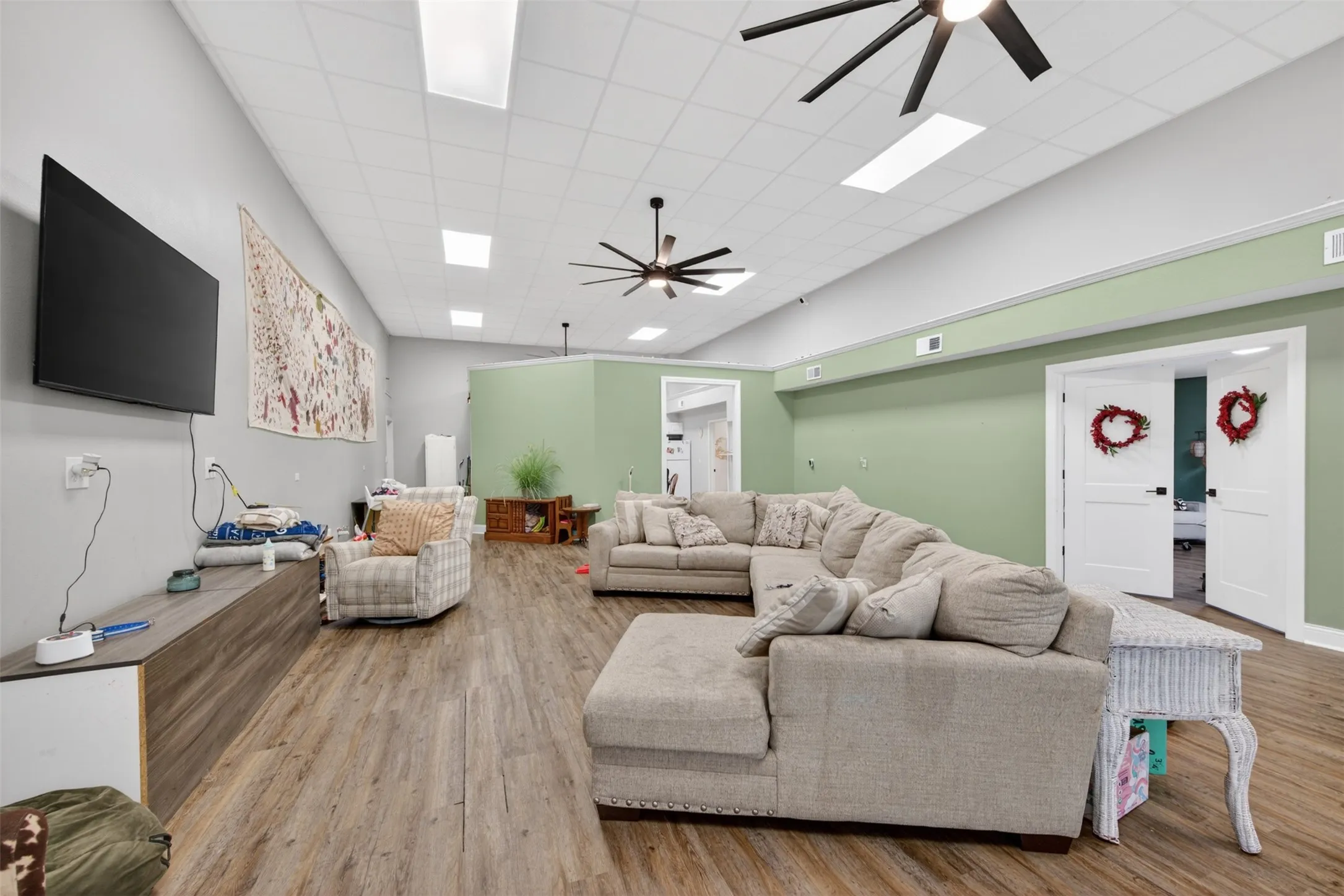 Spacious room featuring wood-finish flooring, a tray ceiling with recessed lighting and ceiling fans, and two sets of white double doors