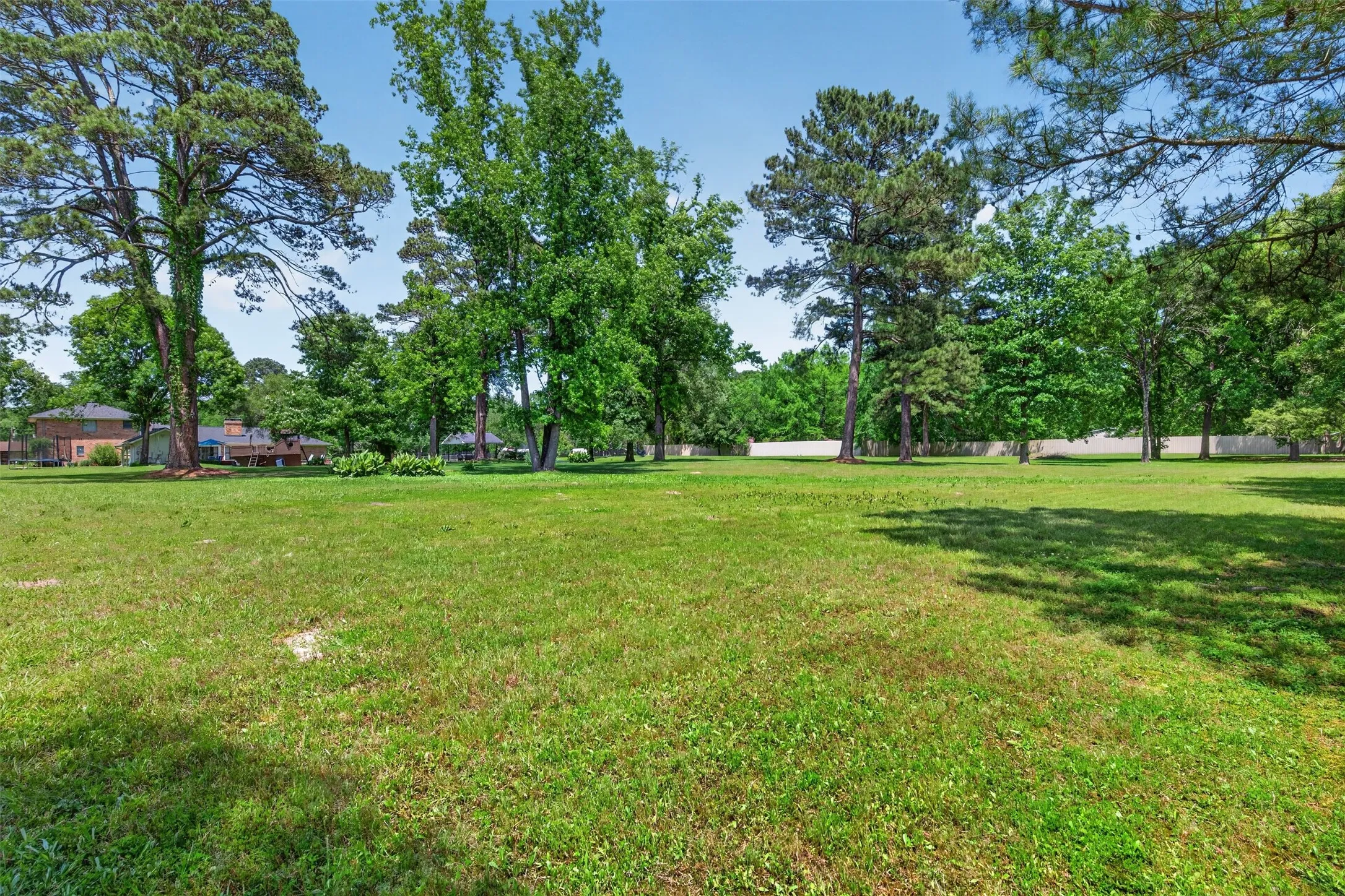 Expansive green lawn with mature trees and a partial white fence in the background