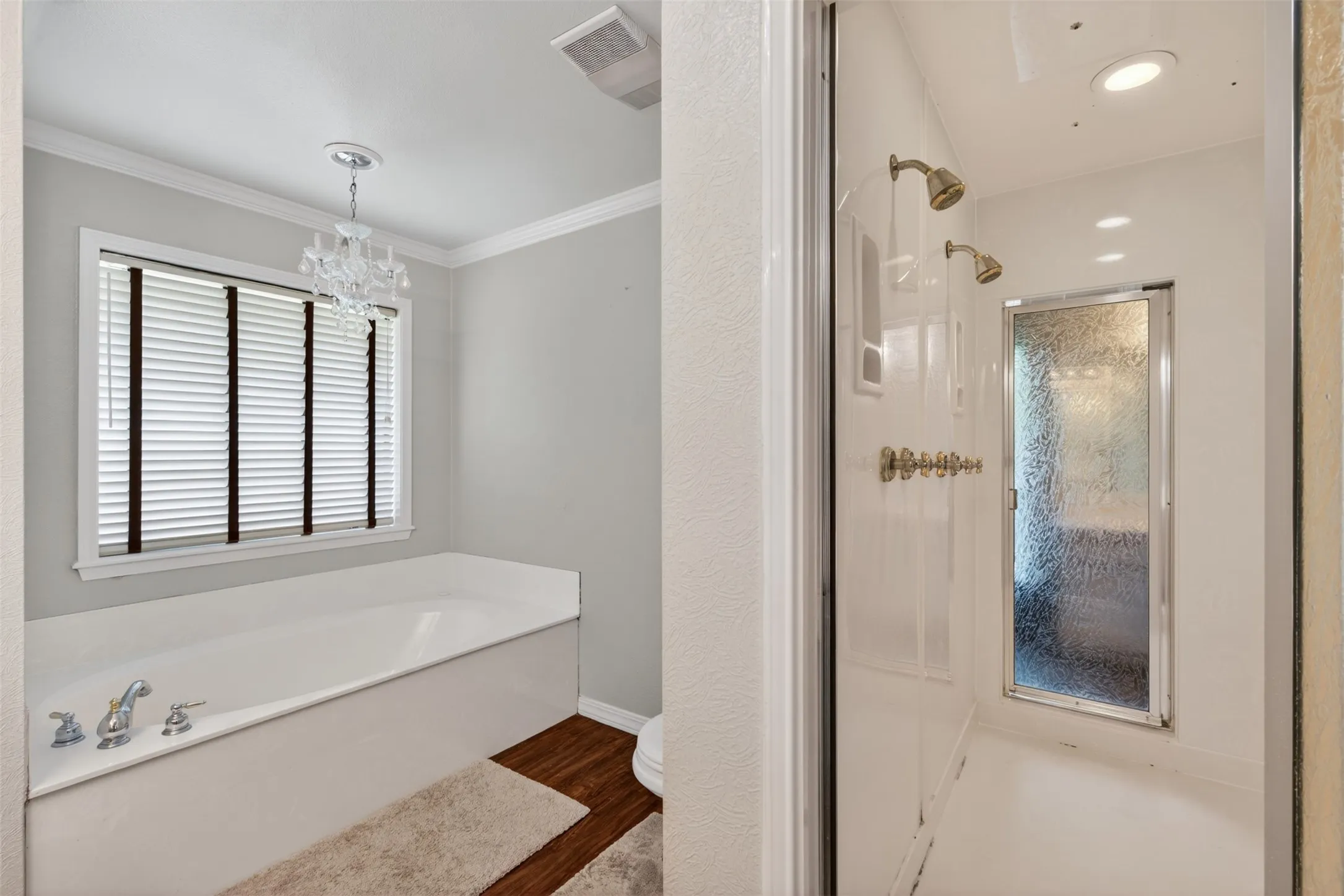 White drop-in bathtub with chrome fixtures, wood-finish flooring, and a crystal chandelier