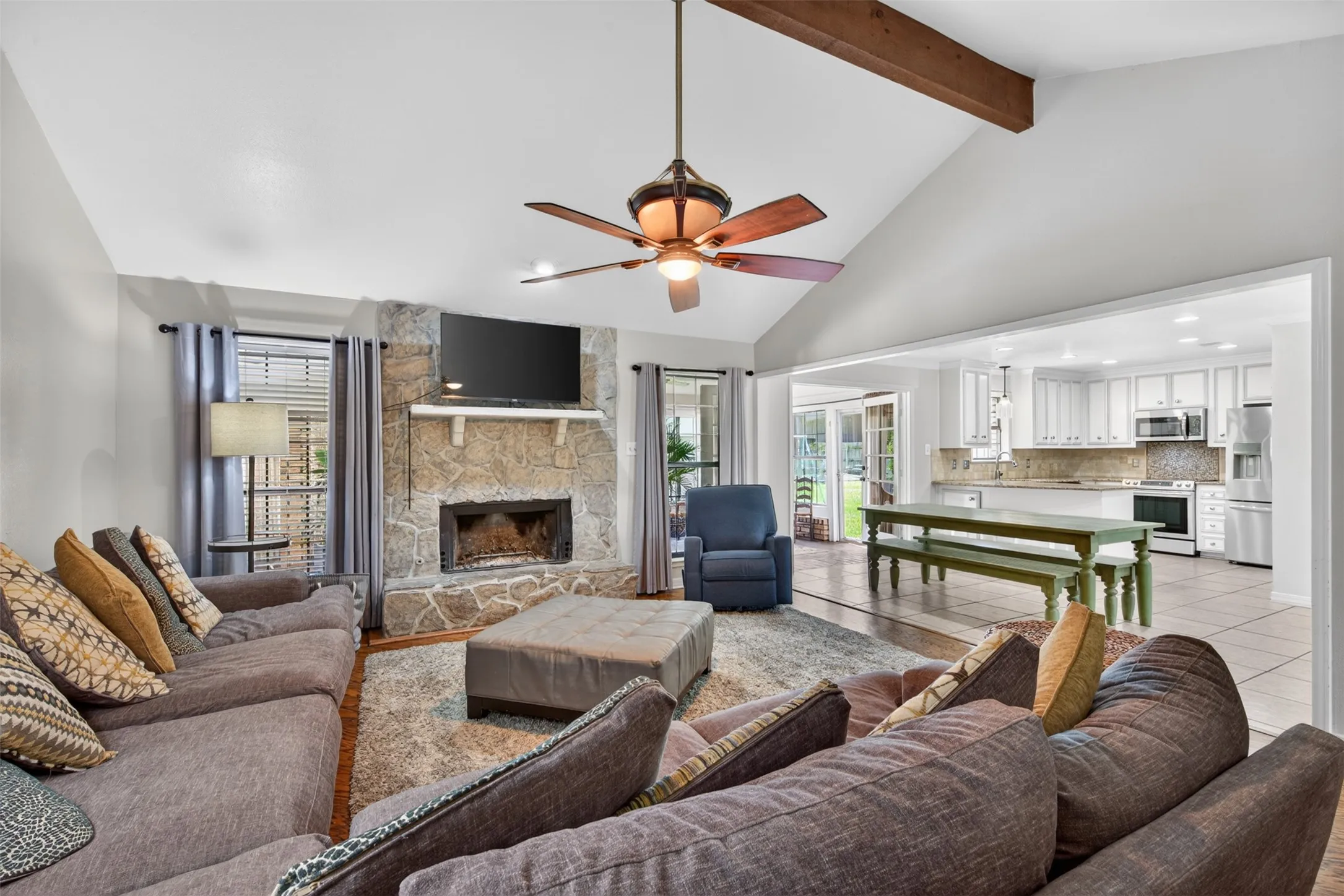 Living area featuring a vaulted ceiling with exposed wood beam, wood-finish flooring, and a stone-faced fireplace