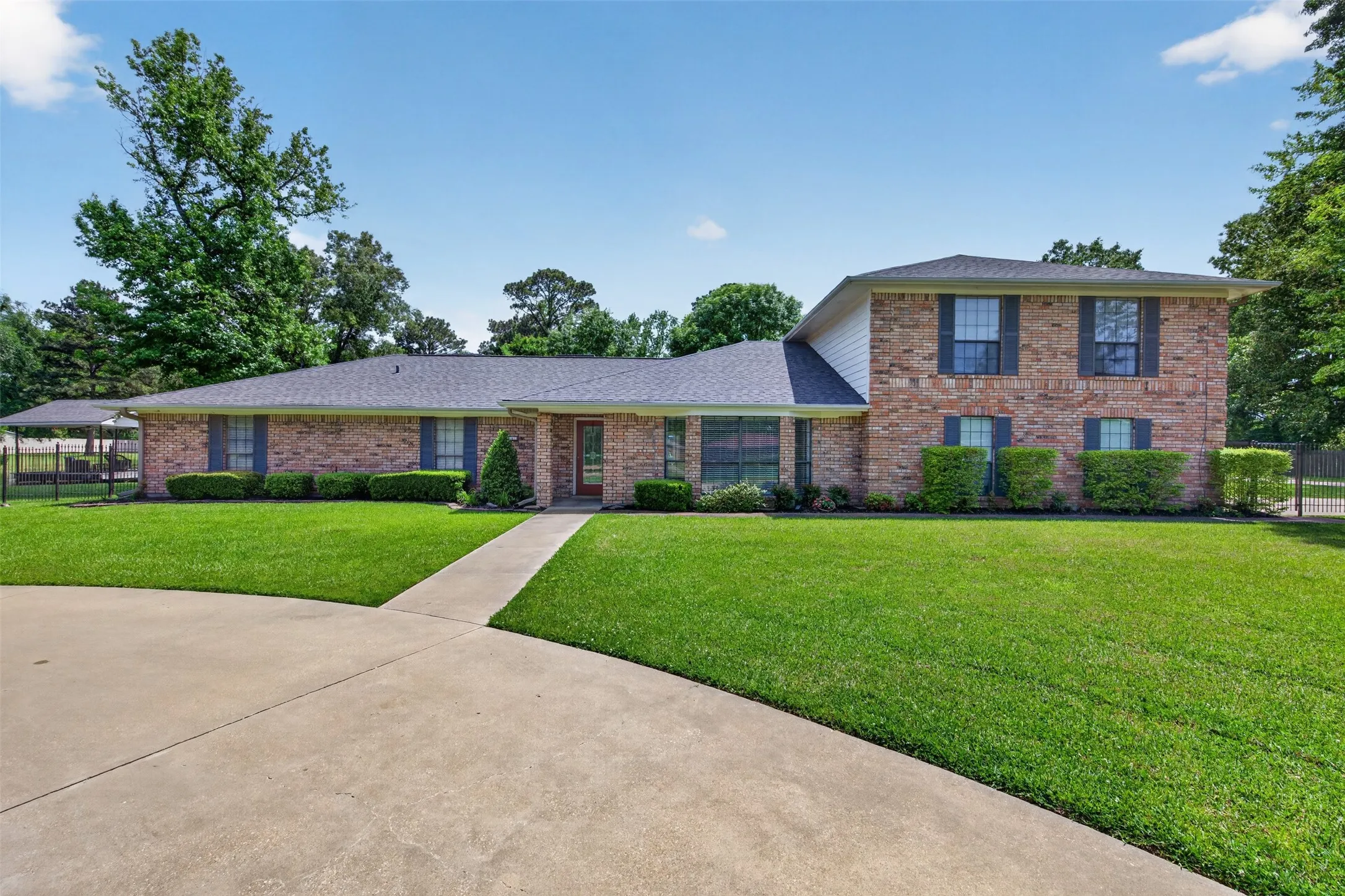 Traditional brick residence featuring a concrete driveway, a walkway leading to the front entry, a dark shingle roof, and established landscaping