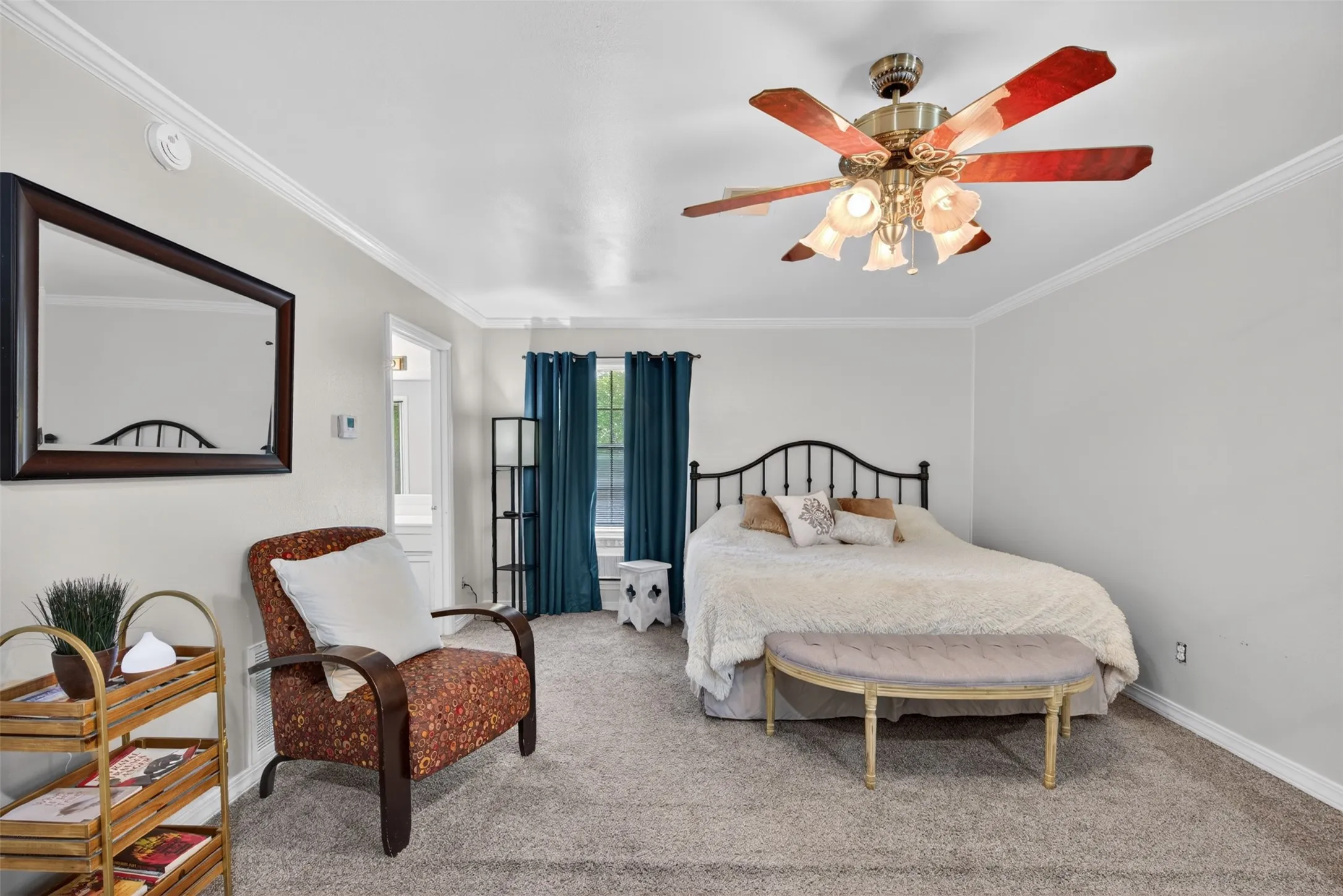 Carpeted bedroom with a ceiling fan light fixture, crown molding, and dual windows draped with teal curtains