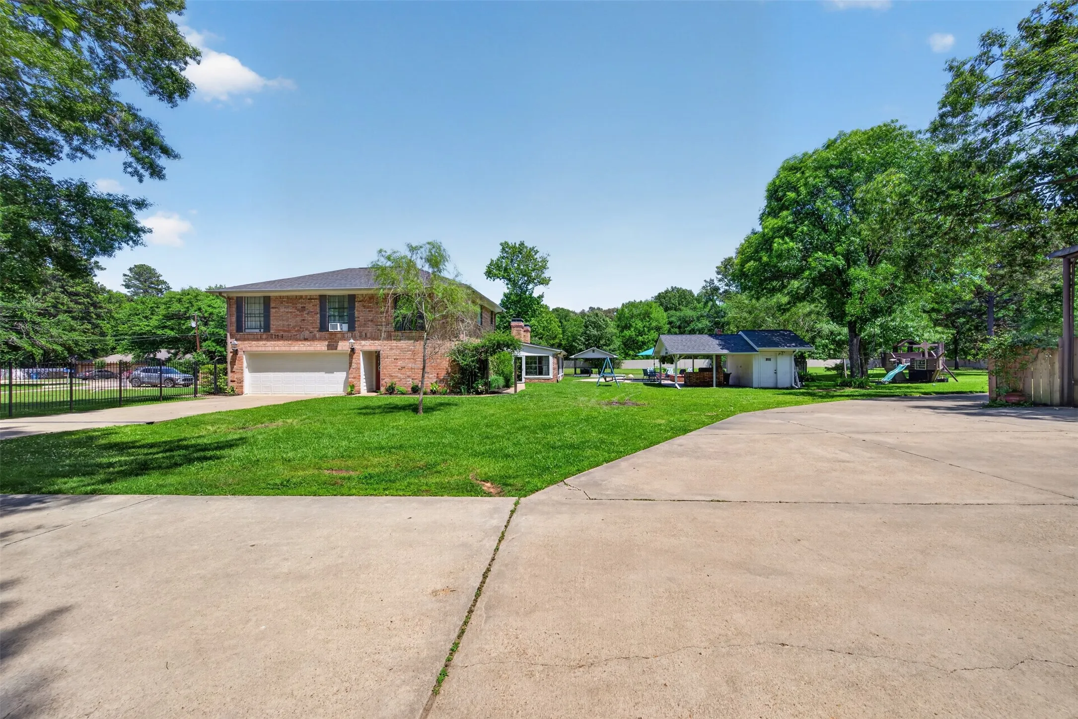 Brick exterior residence featuring a two-car garage, mature landscaping, and an expansive paved driveway