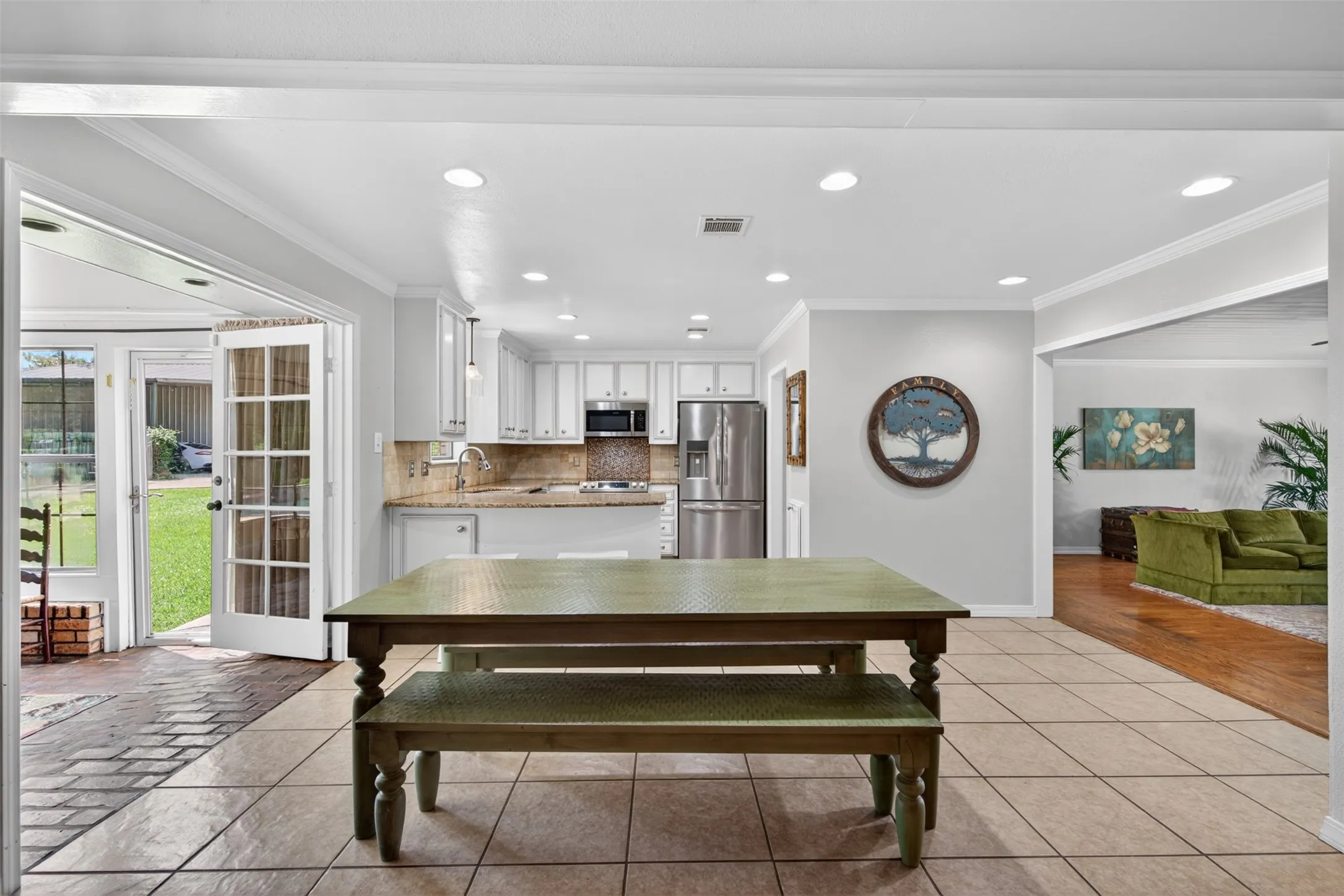 Spacious dining area with tile flooring opening to a bright kitchen featuring white cabinetry, stainless steel appliances, and light-toned countertops