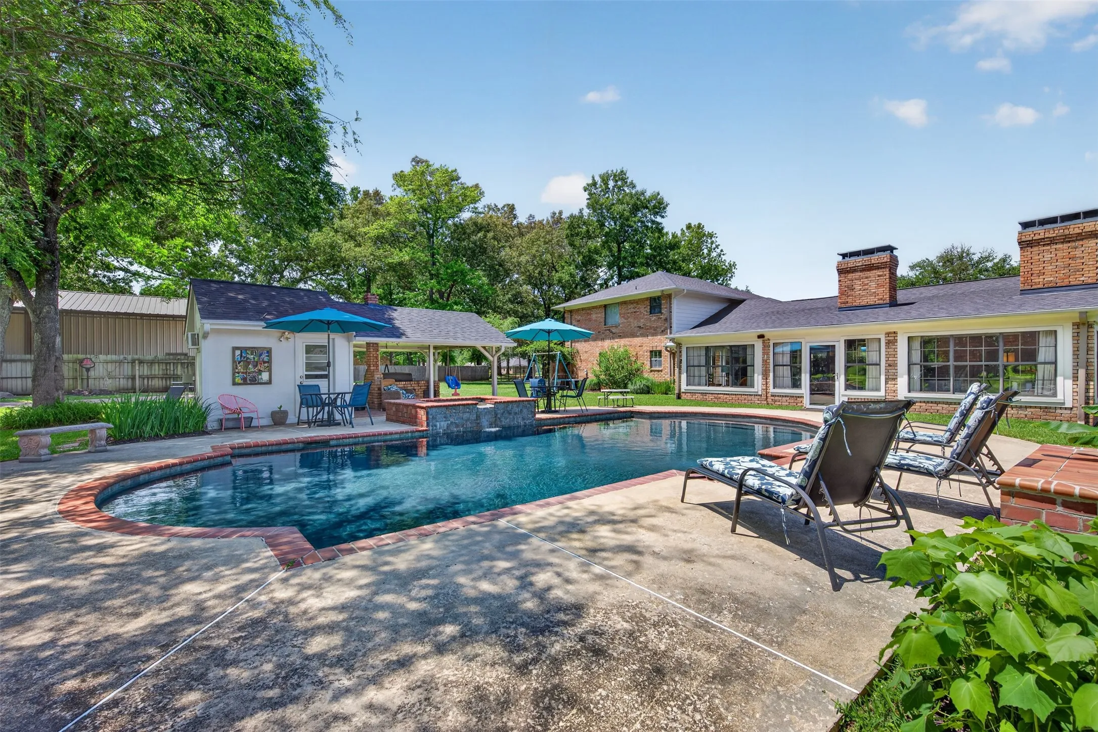 Rear exterior featuring an inground swimming pool, concrete decking, and a brick-capped pool edge