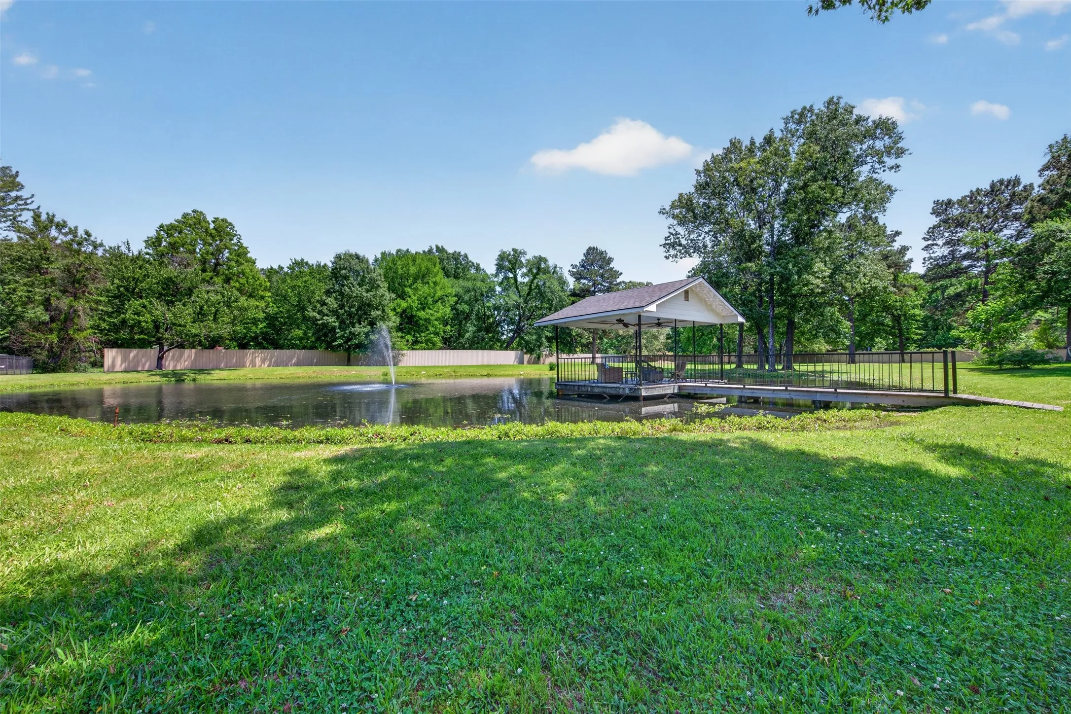 Private pond with a central fountain, bordered by a covered dock and a perimeter fence