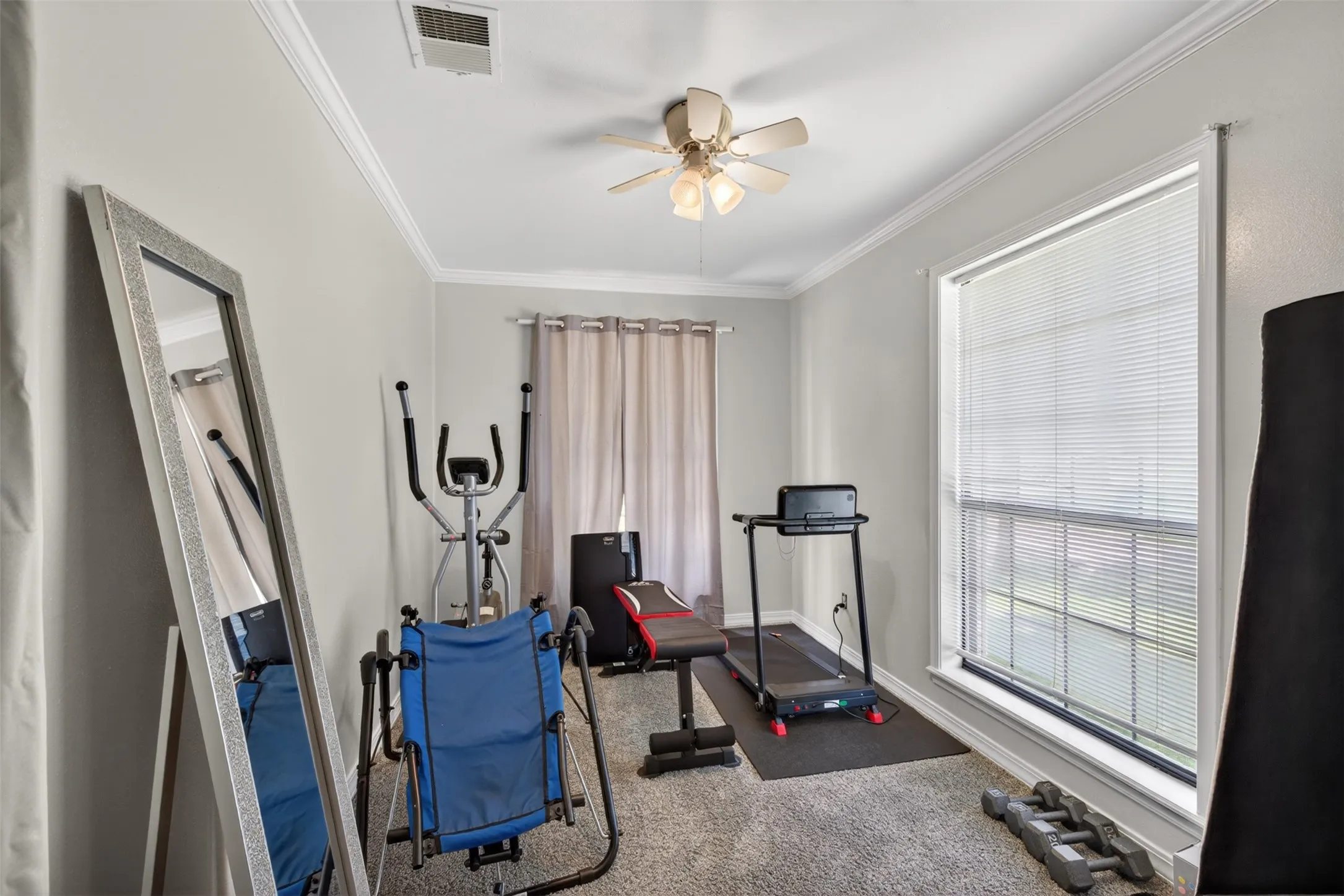 Versatile room featuring light grey wall paint, crown molding, a ceiling fan with light kit, and a large window with blinds
