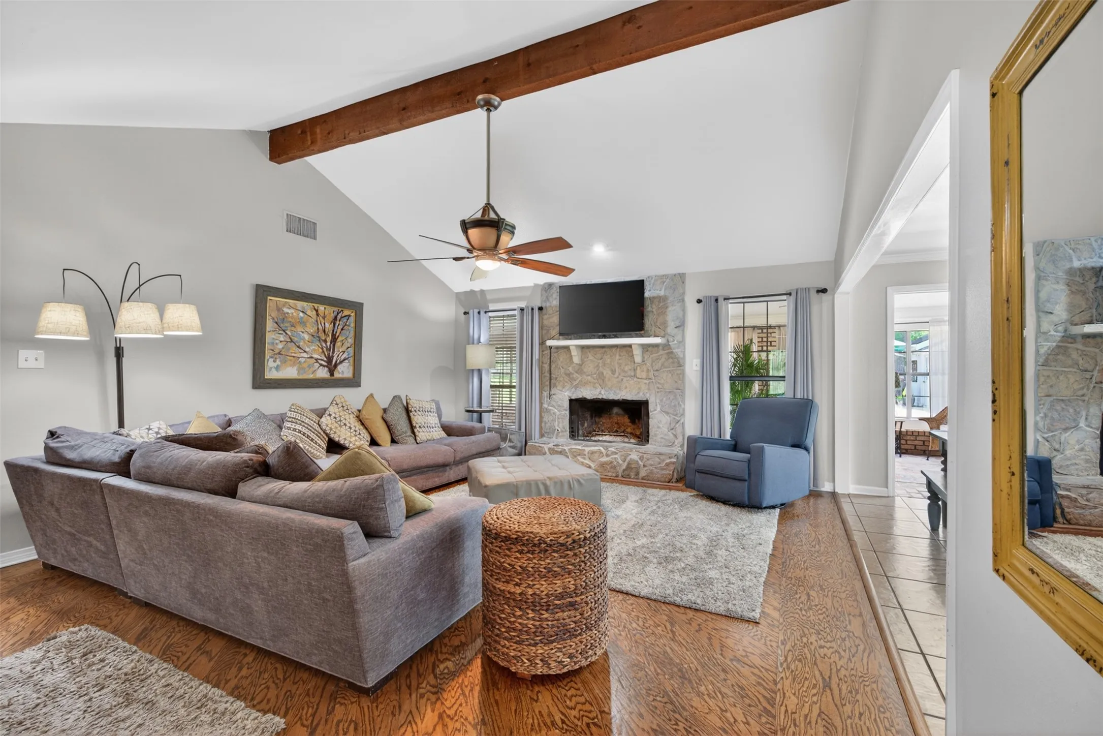 Living area featuring vaulted ceilings with exposed wood beams, a stone-front fireplace, wood-finish flooring, and a ceiling fan