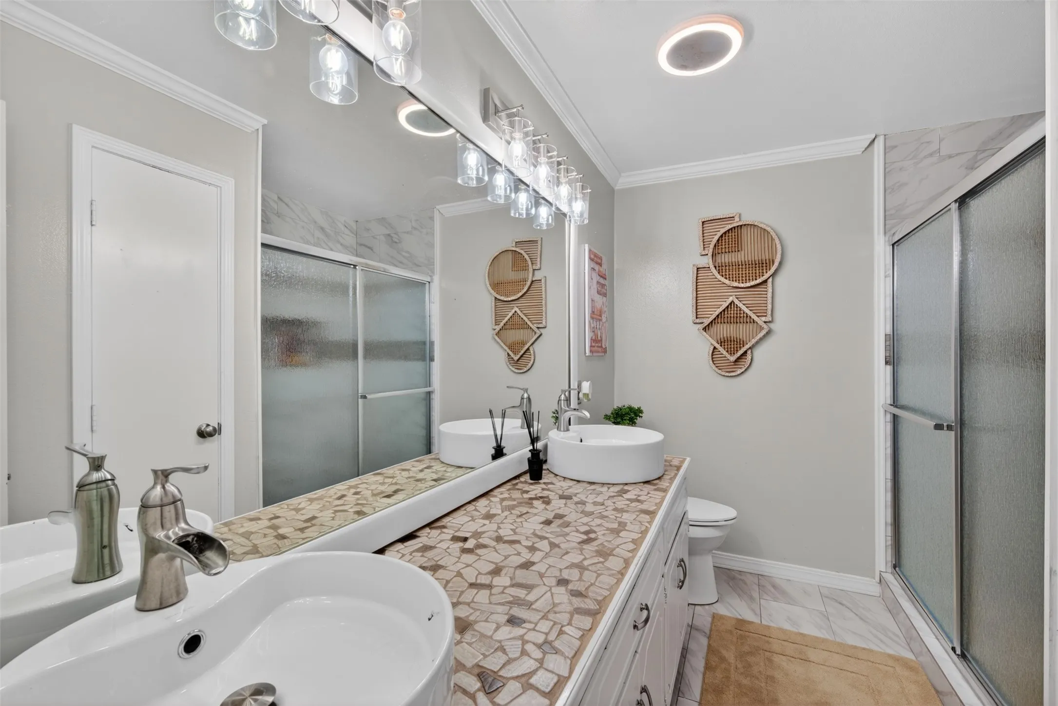 Dual vessel sinks with waterfall faucets set within a mosaic-tiled vanity